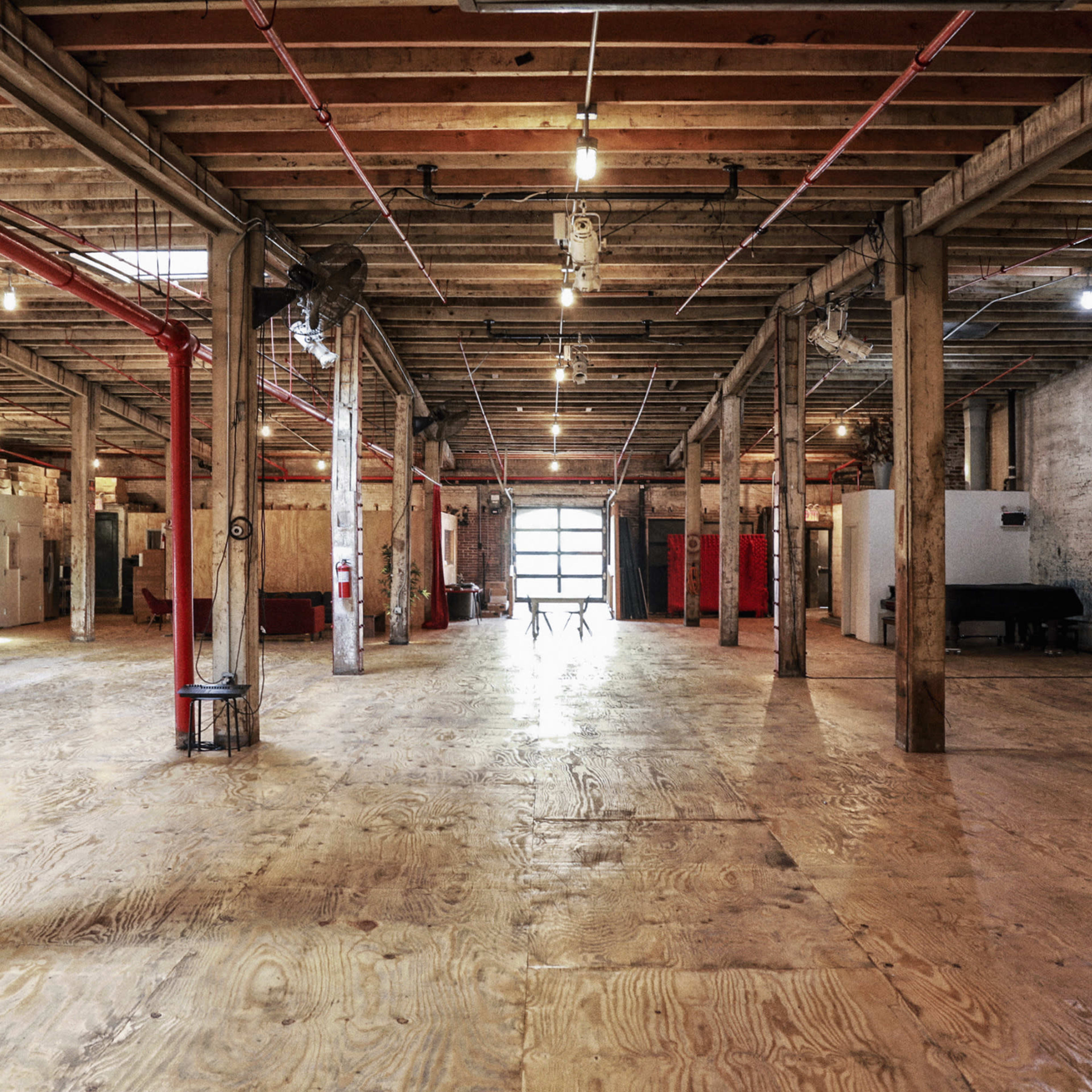 An expansive, empty industrial space with wooden floors and exposed beams, featuring a row of columns and a large rear window letting in light.