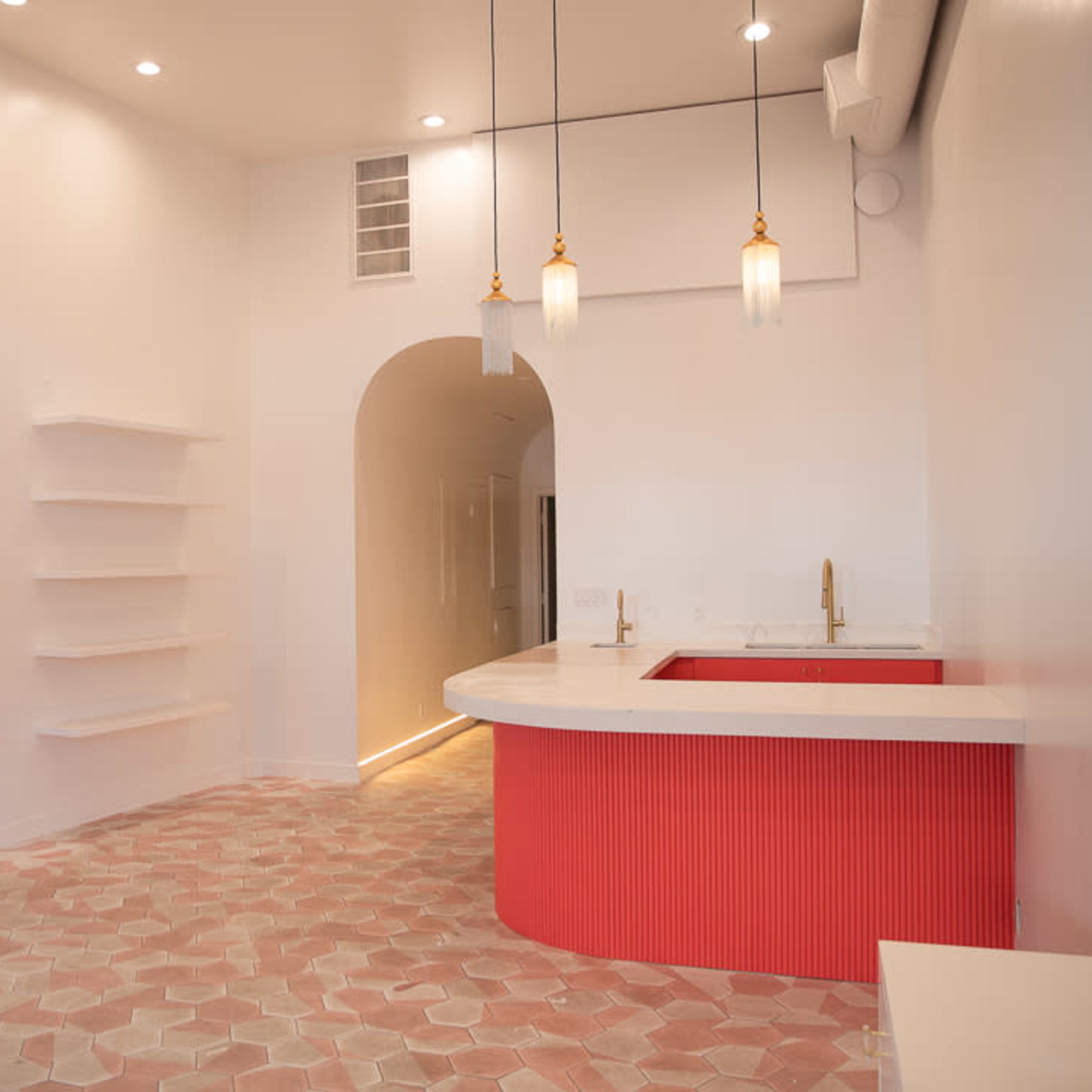 A modern interior space featuring a curved counter with a red accent, light-colored walls, and hexagonal tiled flooring.