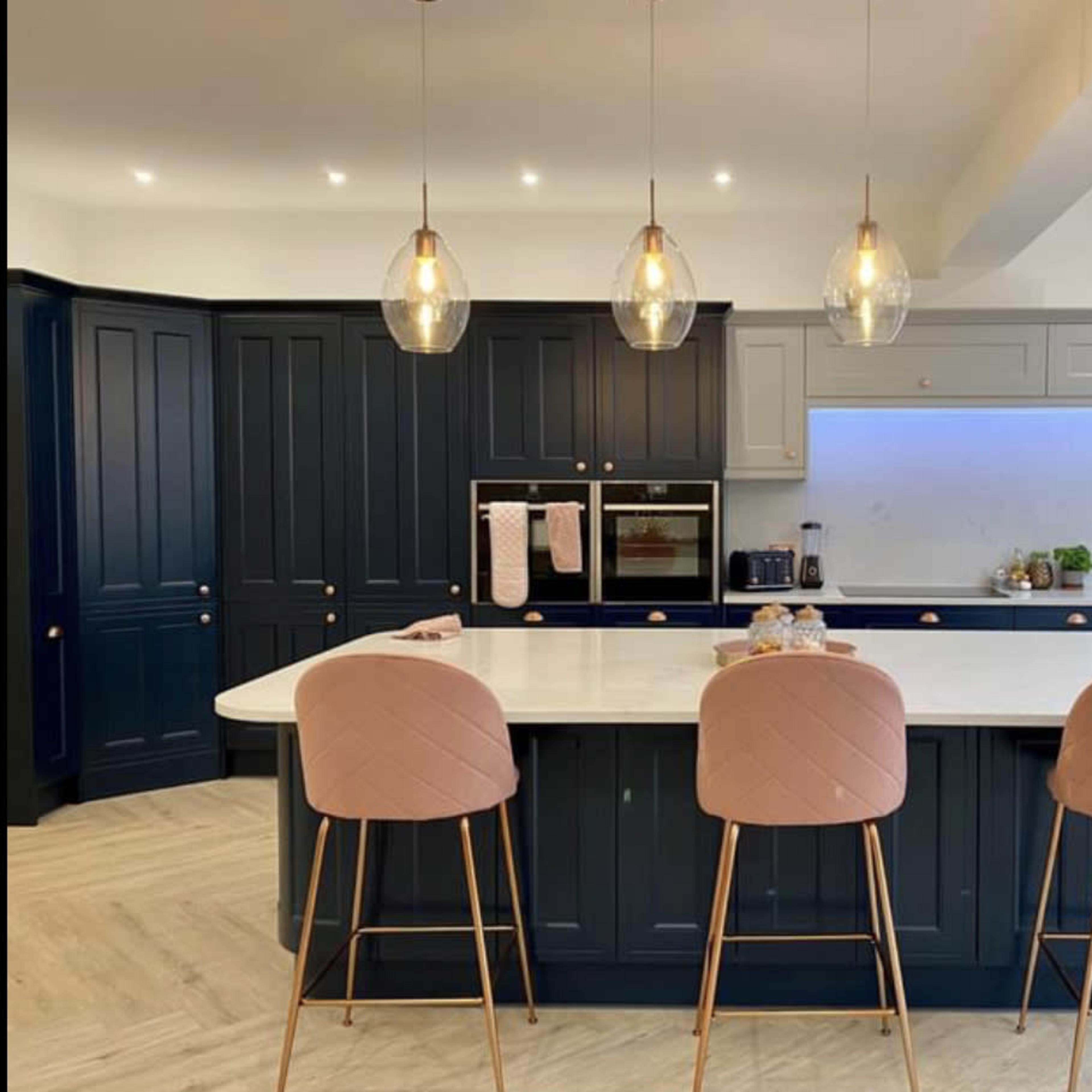 The kitchen features a large island with four bar stools, surrounded by dark blue cabinetry and modern pendant lights.