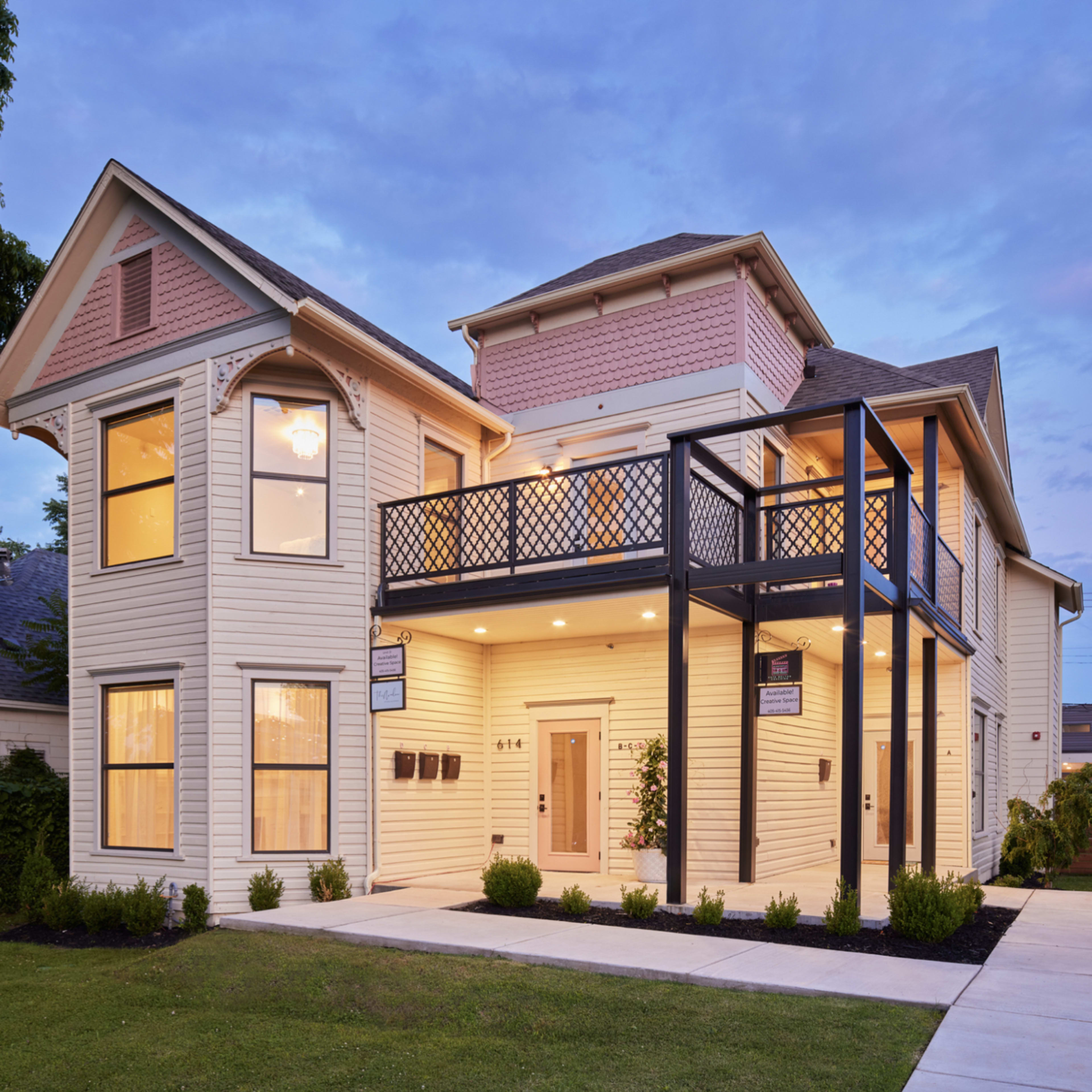A two-story, light-colored house with a front porch, large windows, and a black balcony railing.