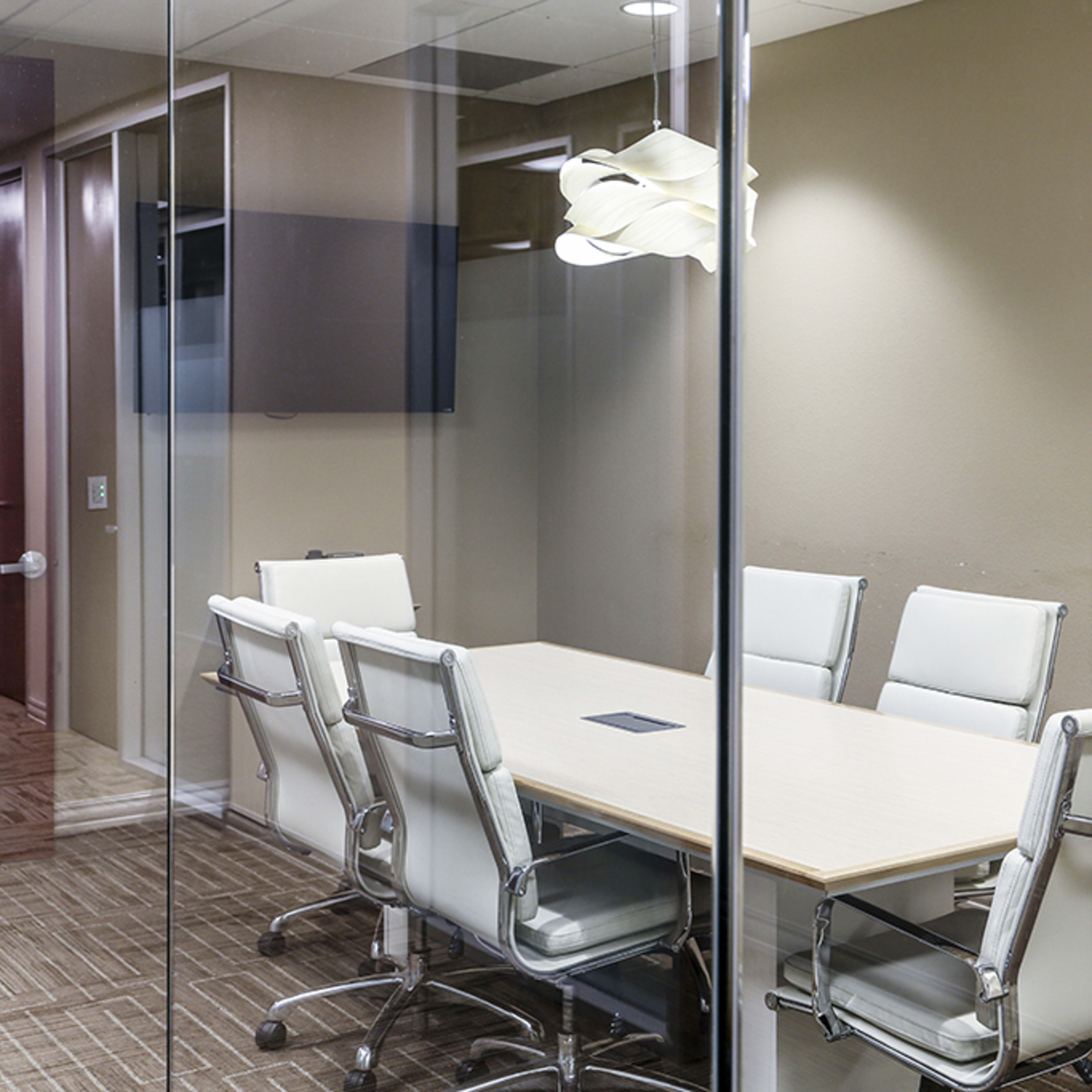 A modern conference room with a long table and several white leather chairs surrounded by glass walls.