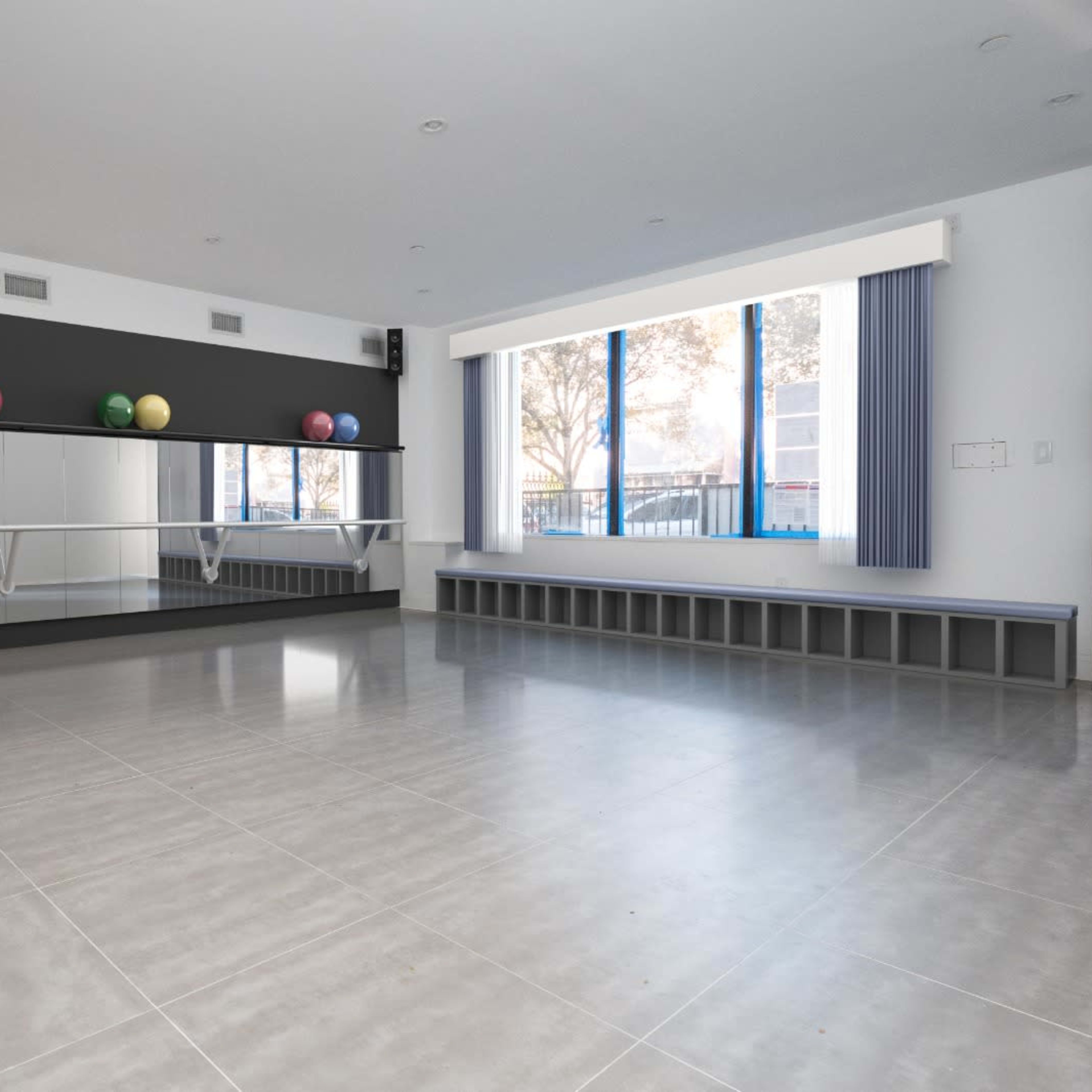 A spacious, empty fitness studio features a mirrored wall, large windows, and several colorful exercise balls scattered on the floor.