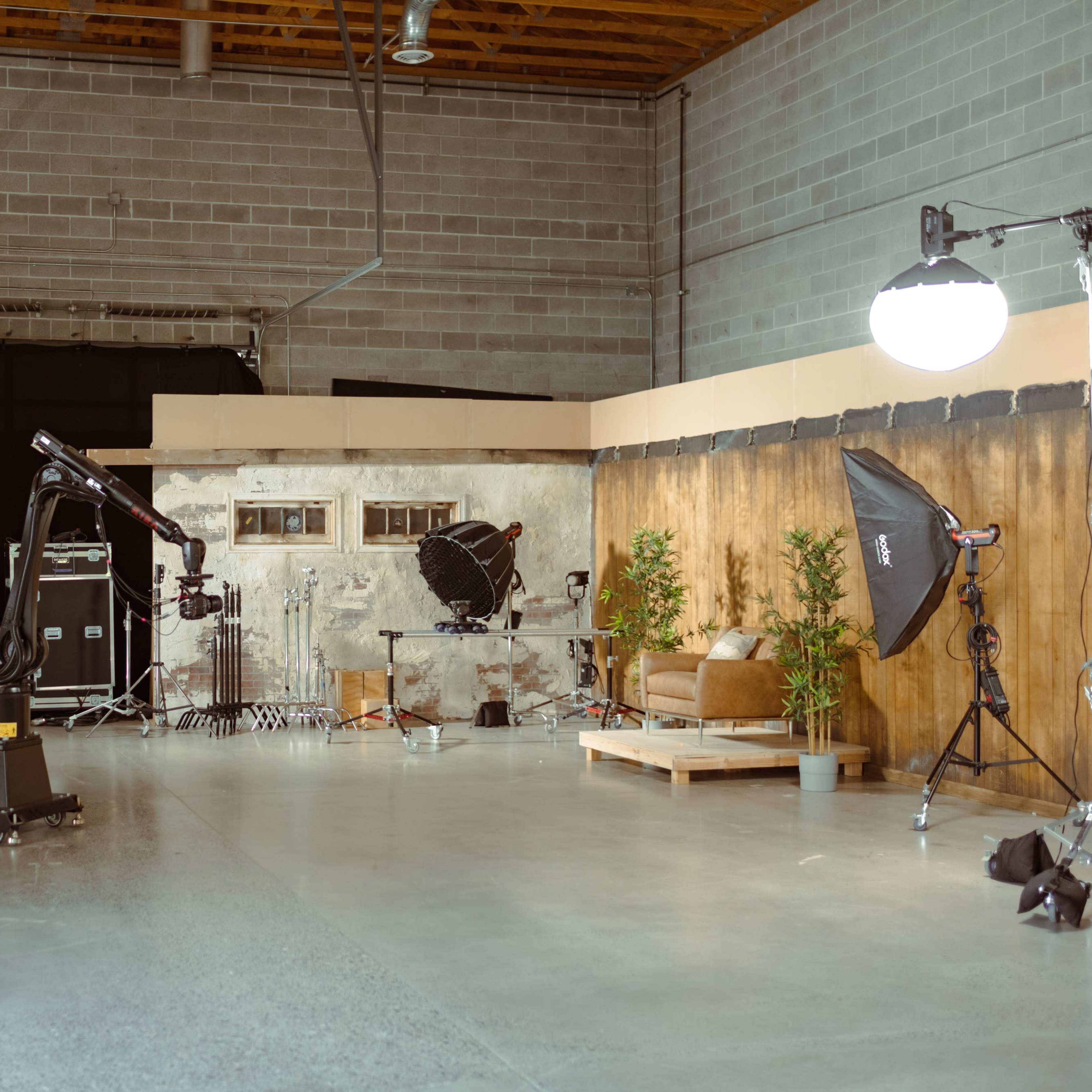 A spacious photography studio features various equipment, lighting setups, and a staged seating area against a neutral backdrop.