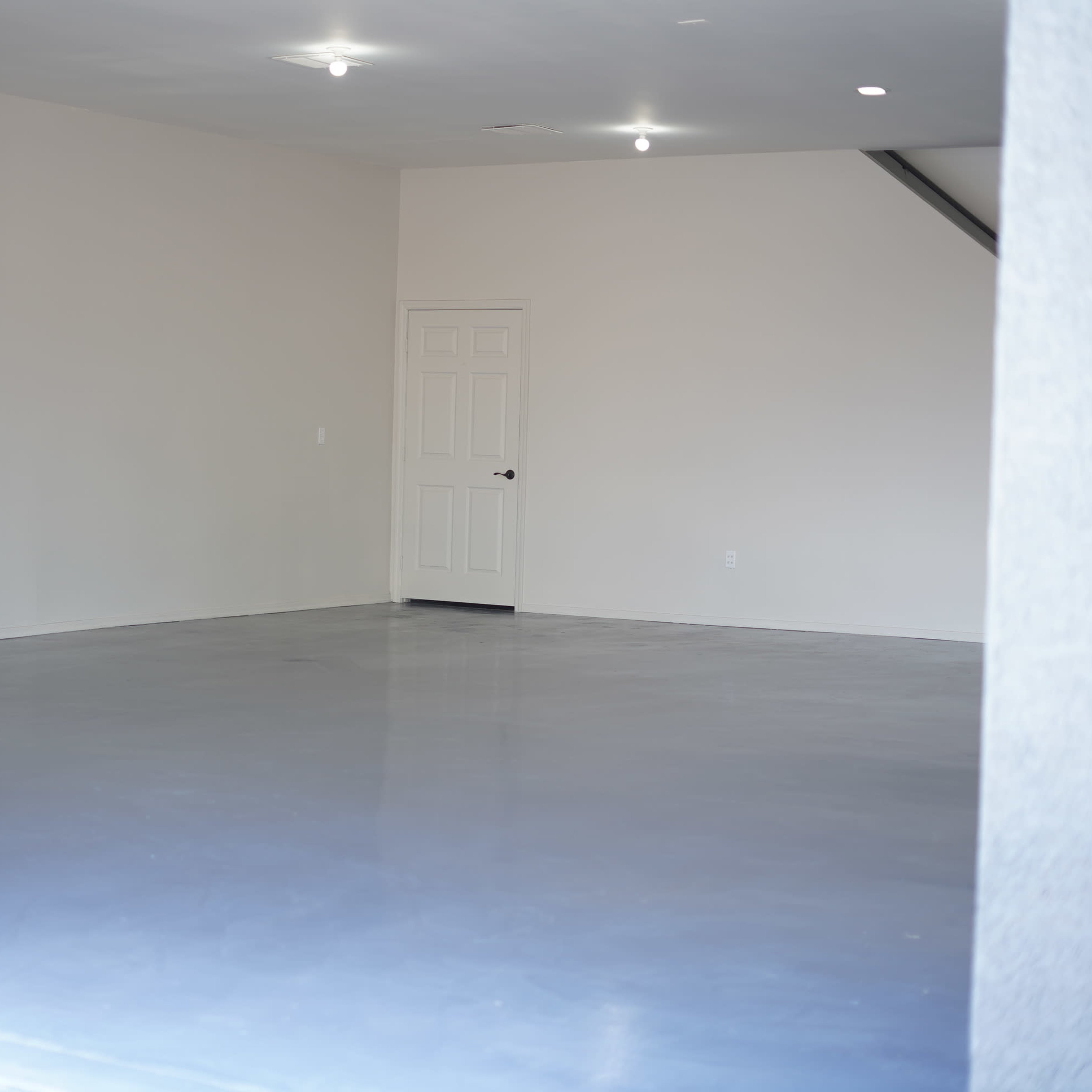 An empty room with a concrete floor, plain walls, and a single door at the back.
