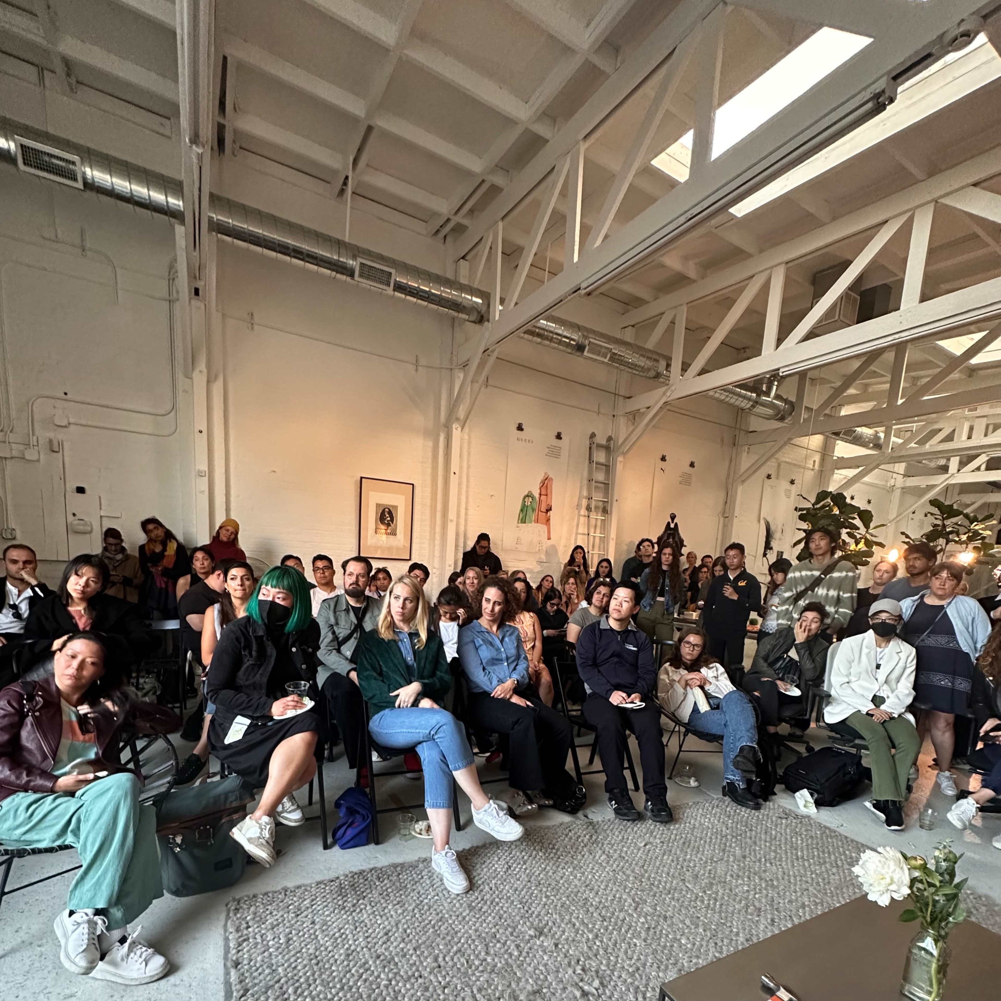 A large group of people is seated in a well-lit room, focusing on a presentation in front of them.
