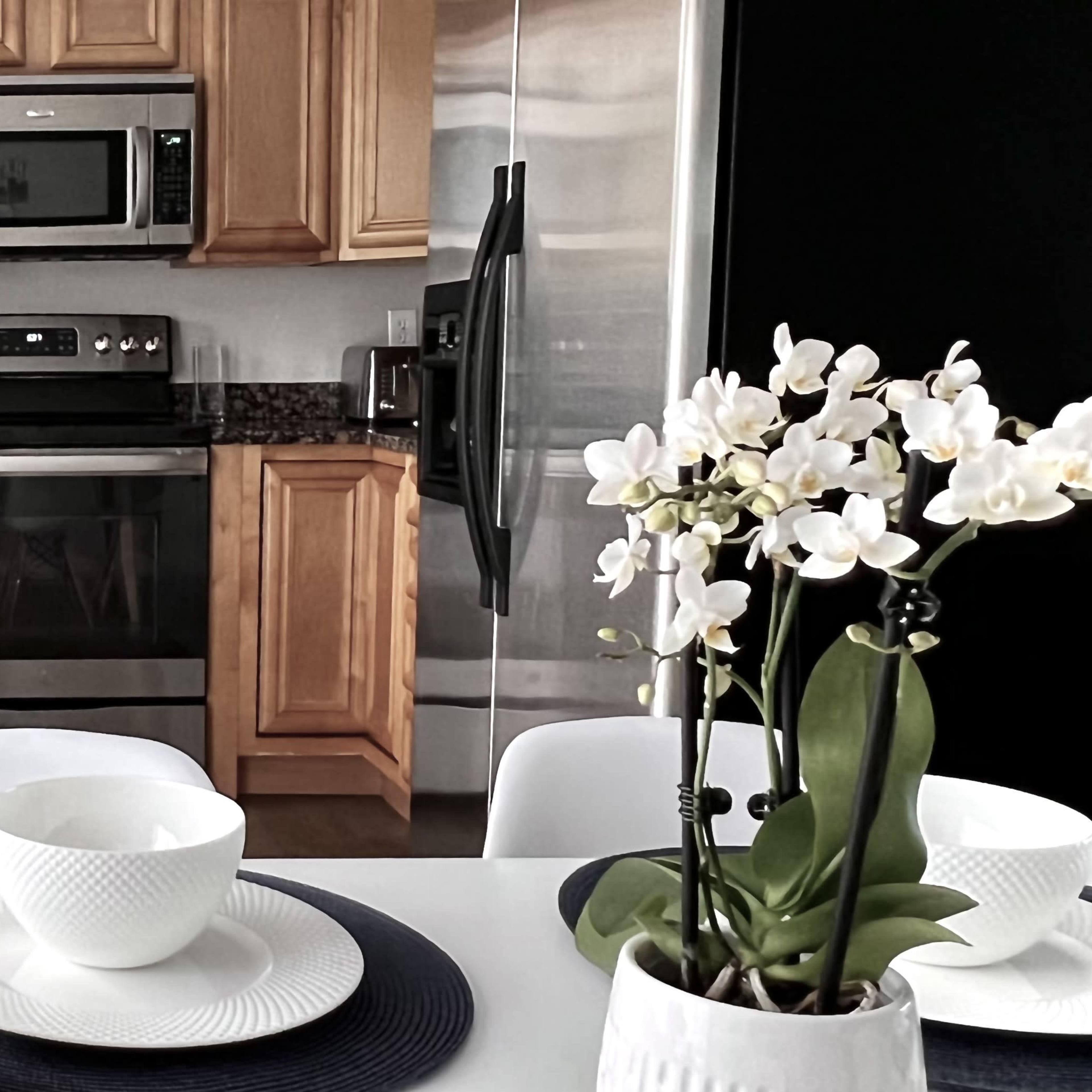 A modern kitchen featuring wooden cabinetry, stainless steel appliances, and a table set with fruit and tableware.
