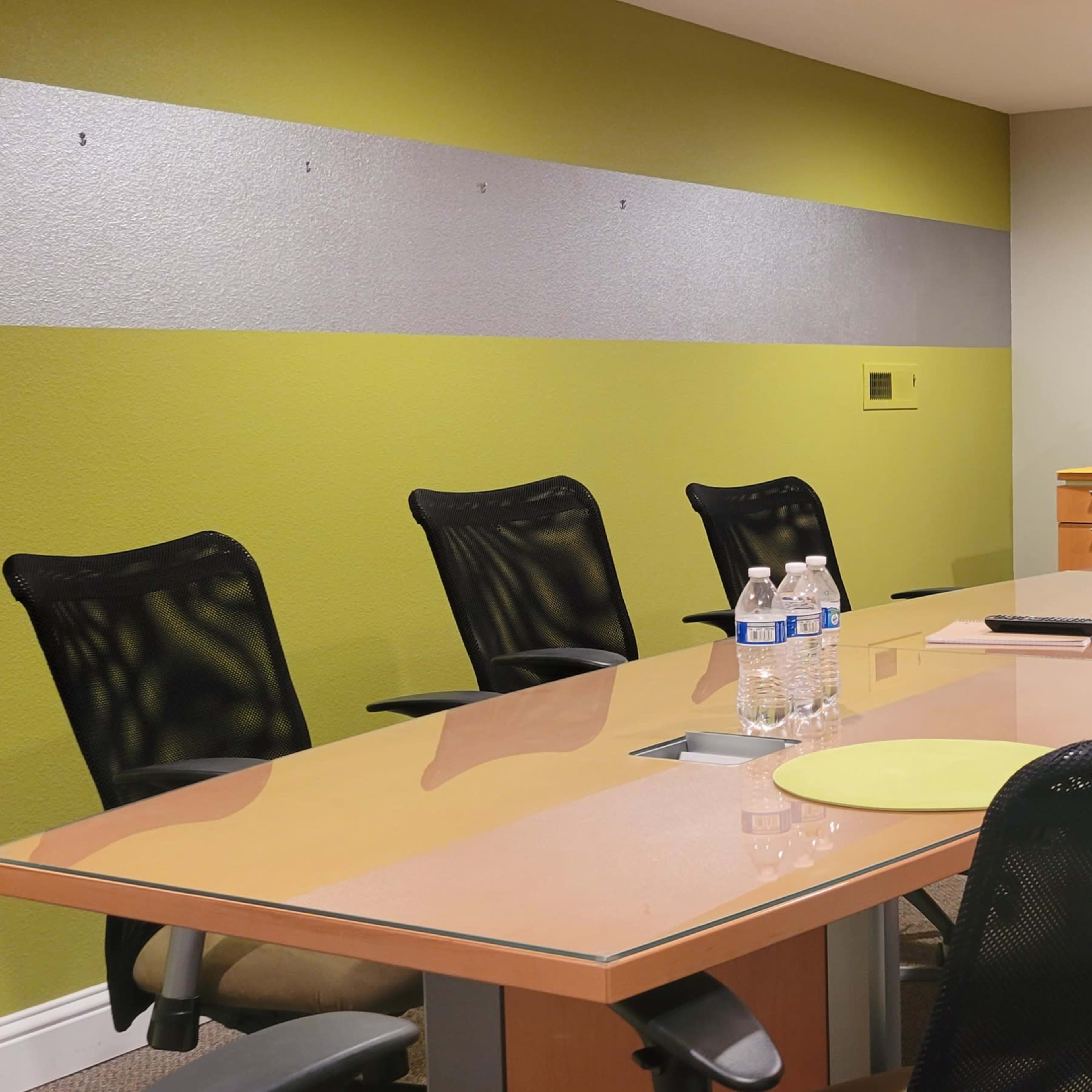 A modern conference room features a large table surrounded by black chairs, with a television mounted on the wall and a side cabinet.