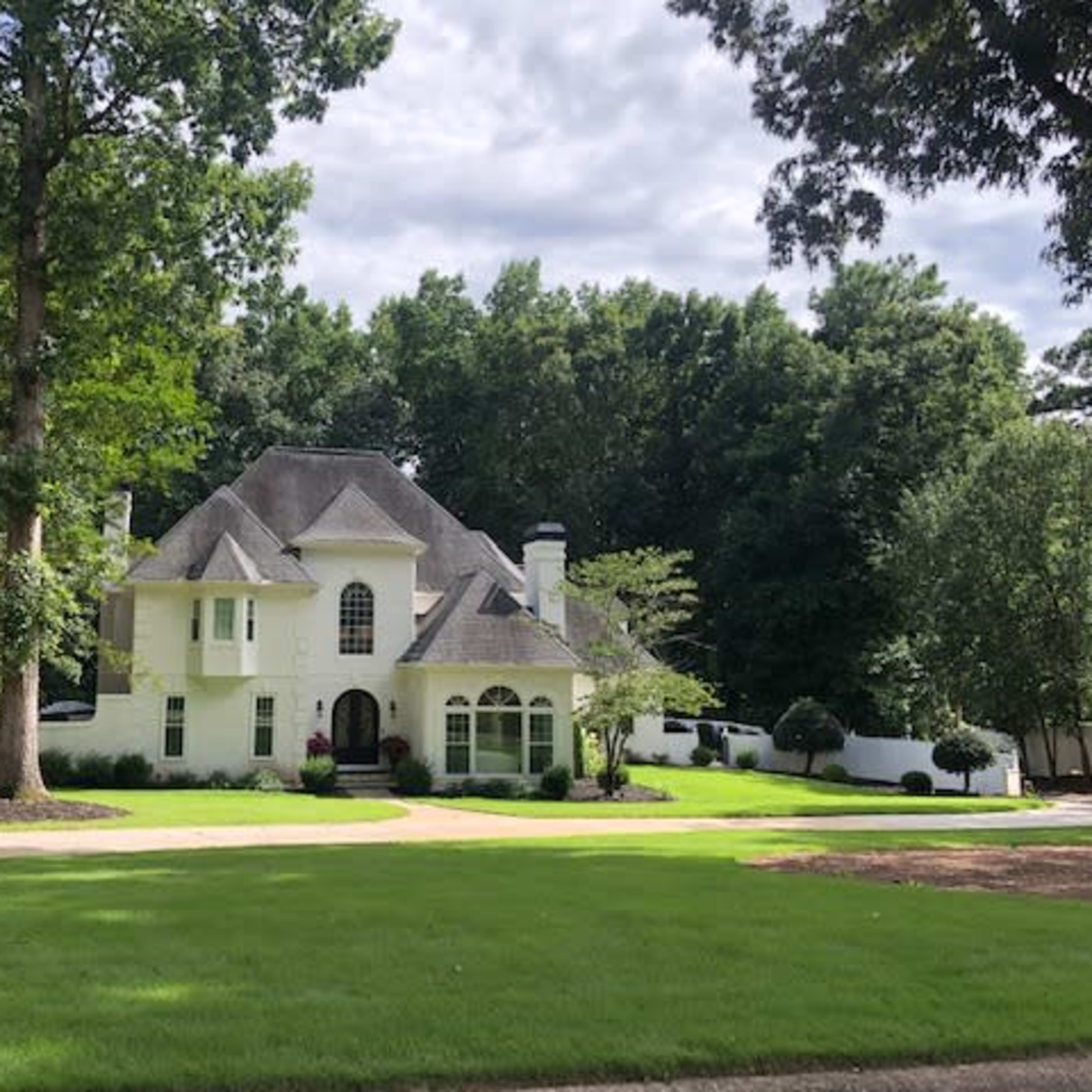 A large white house with a gray roof is set among tall trees and manicured lawns.