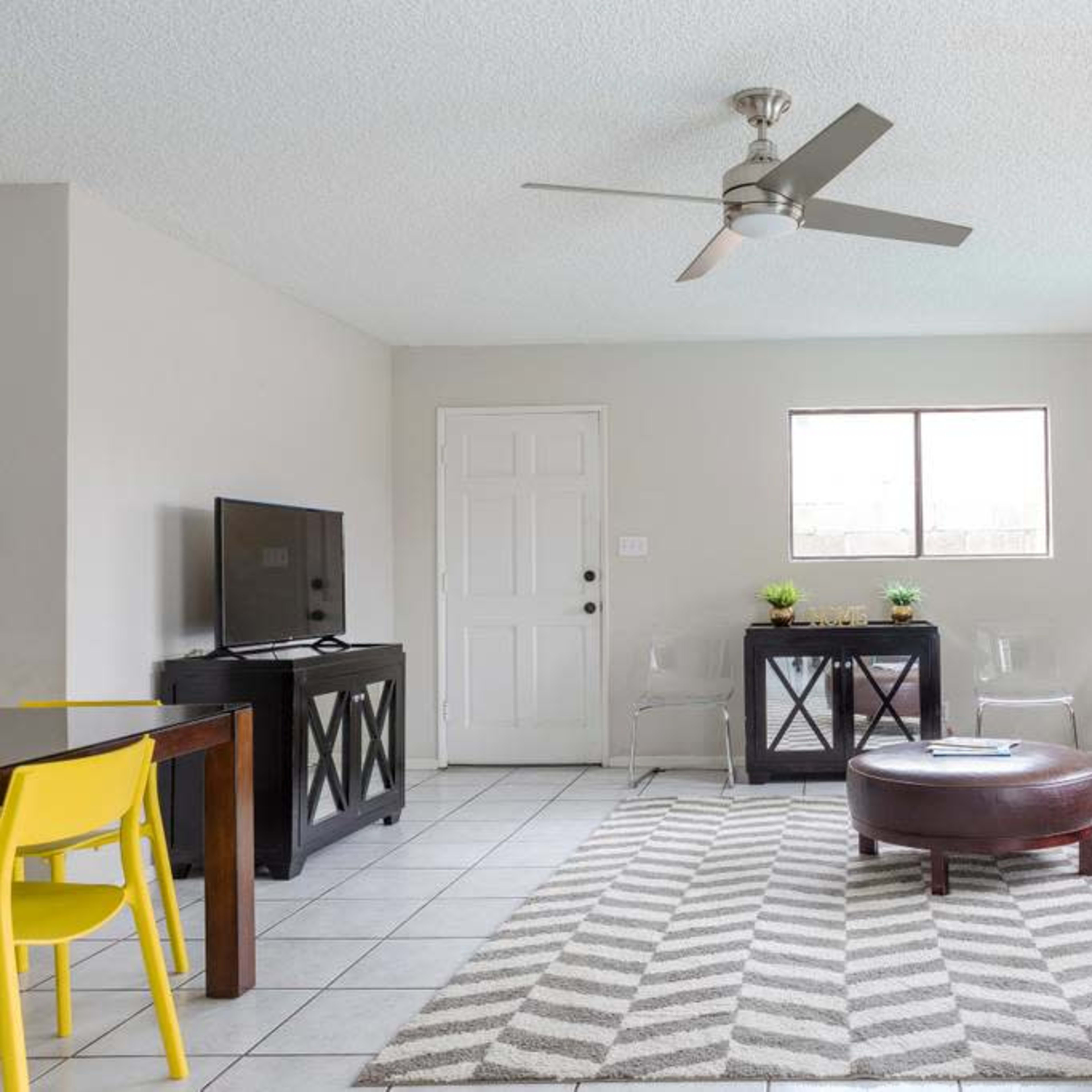 A living room with a sofa, a coffee table, a television, and a dining area with a yellow chair.