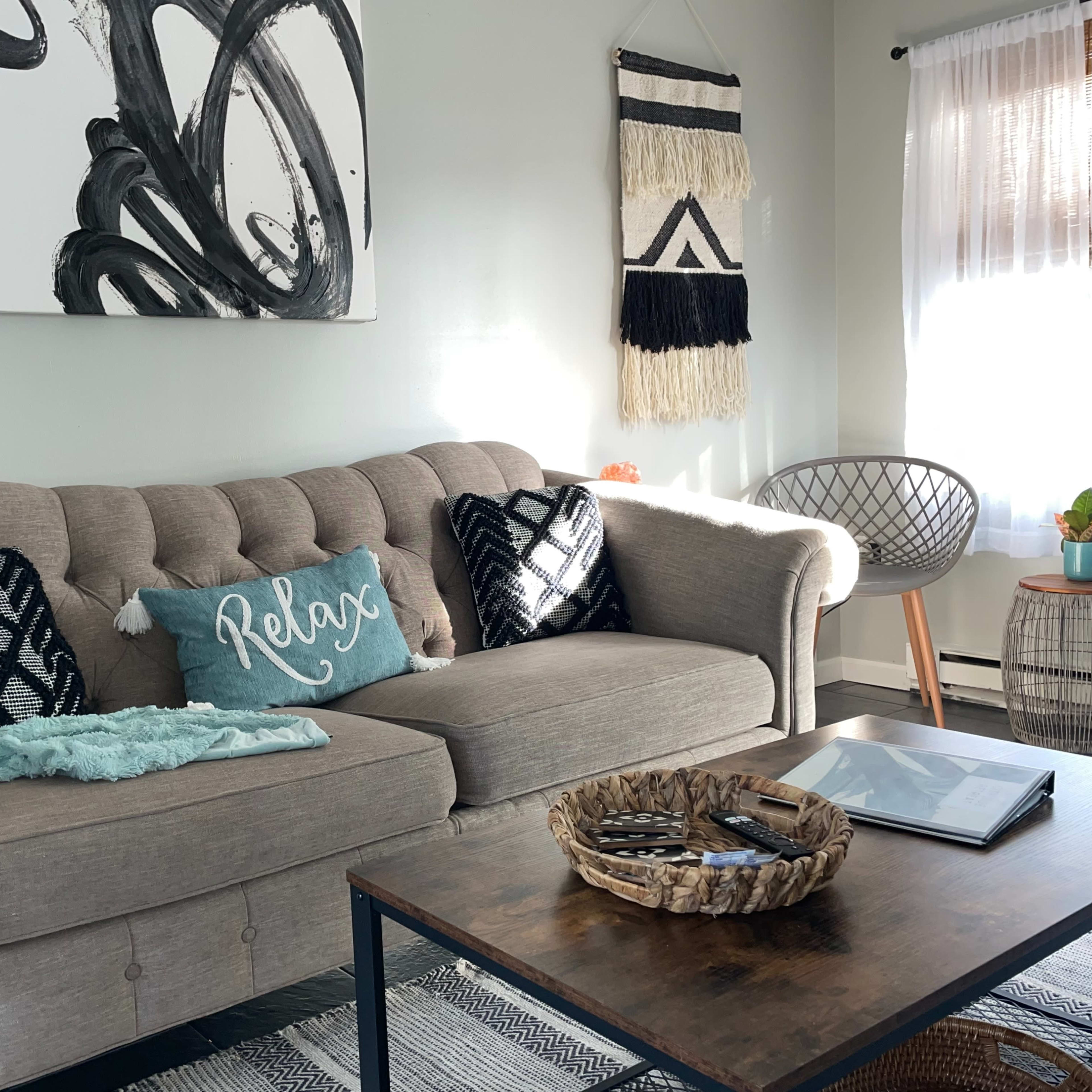 A cozy living room with a tufted beige sofa, decorative pillows, a wooden coffee table, and sunlight filtering through a window.