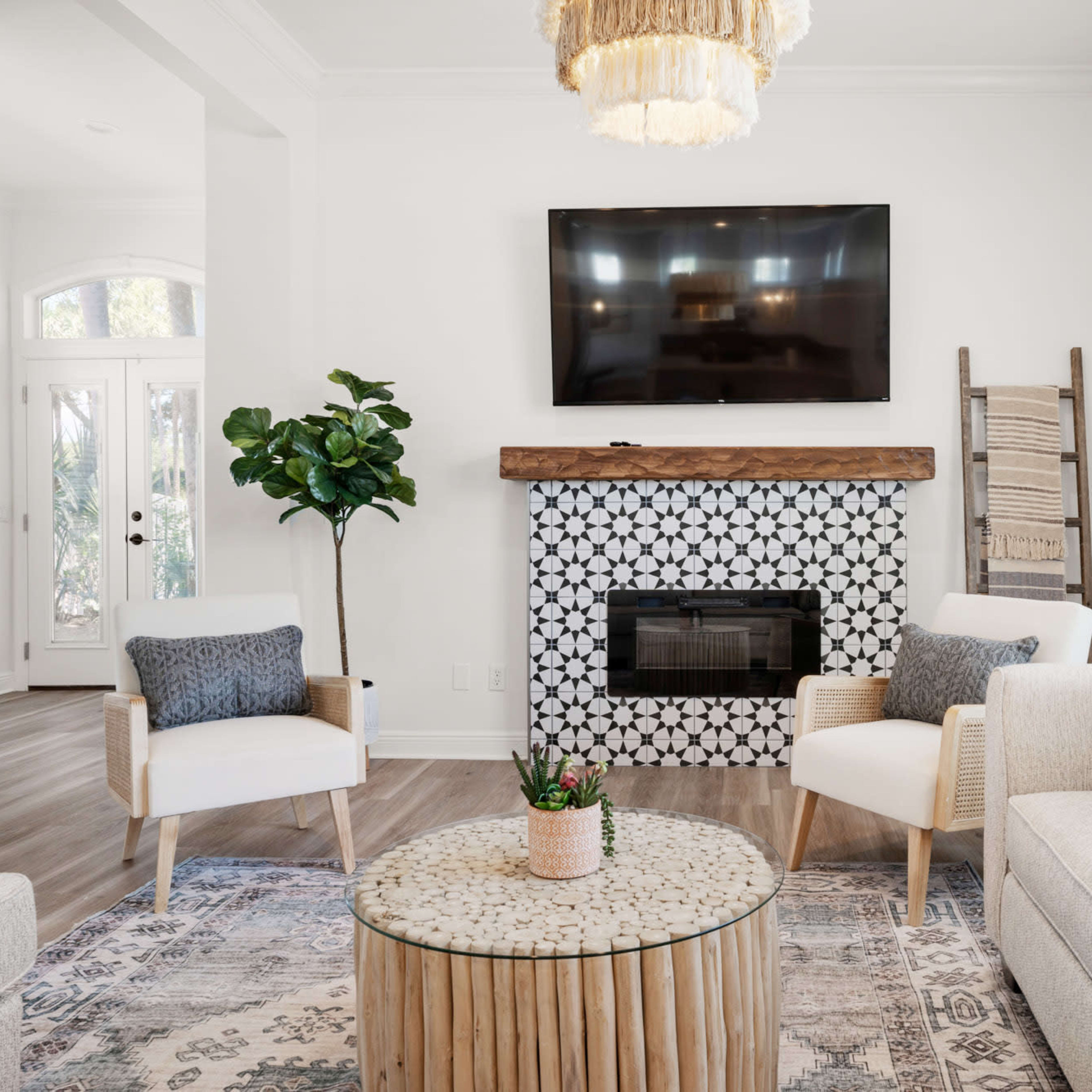The scene features a bright living room with a television mounted above a decorative fireplace, surrounded by light-colored furniture and a circular coffee table.