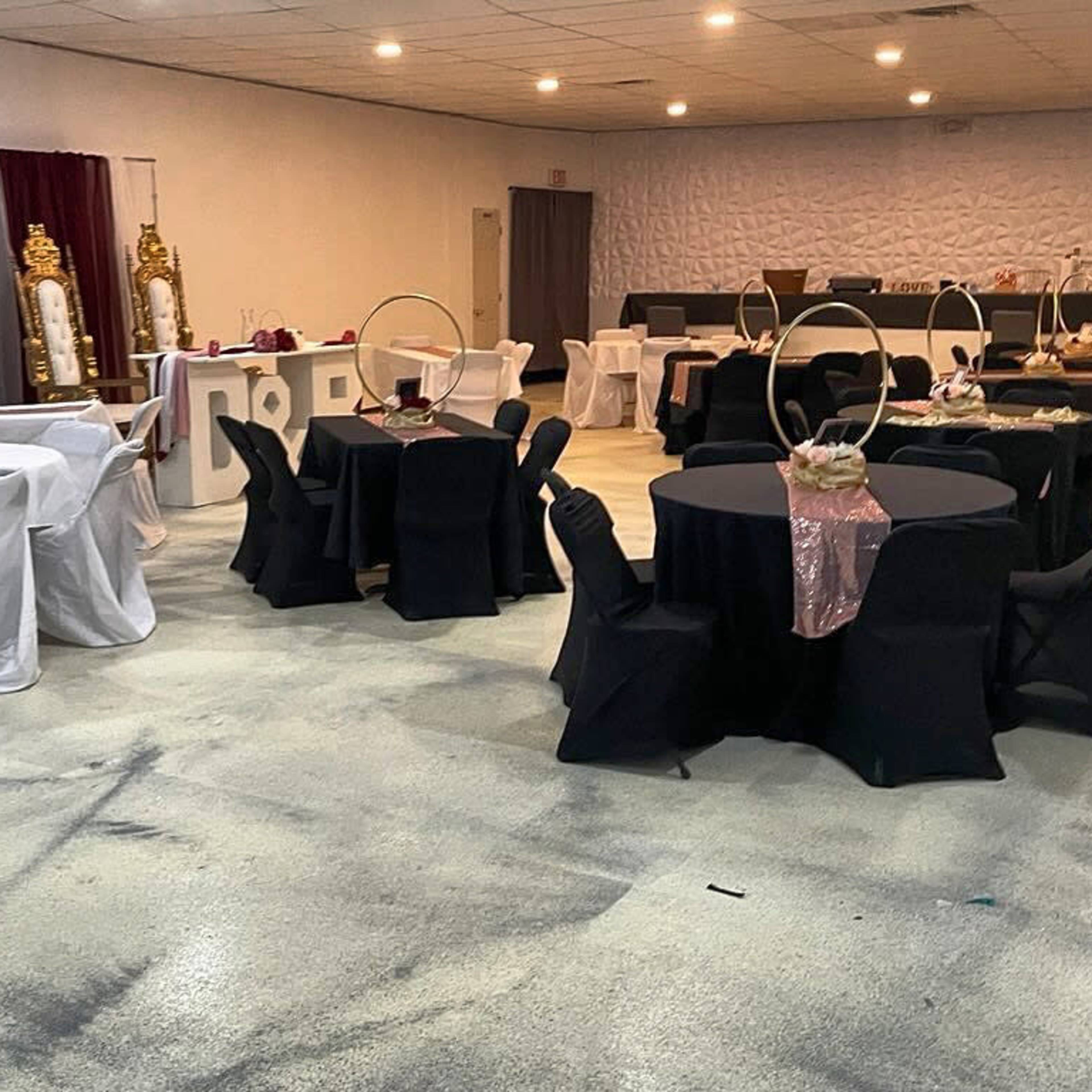 A spacious event hall arranged with multiple round tables covered in black and white tablecloths.