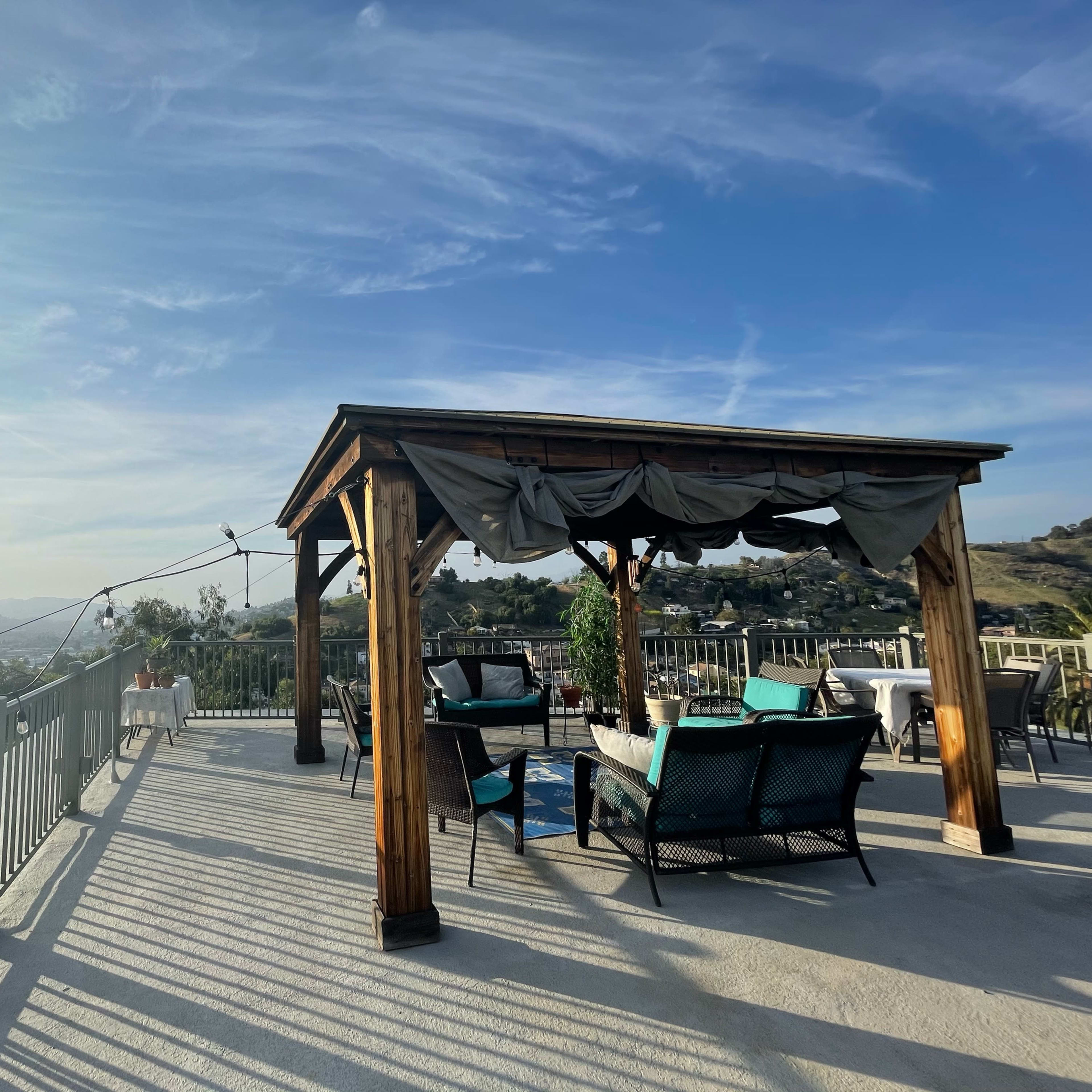 A wooden pergola with seating overlooks a valley under a clear sky.