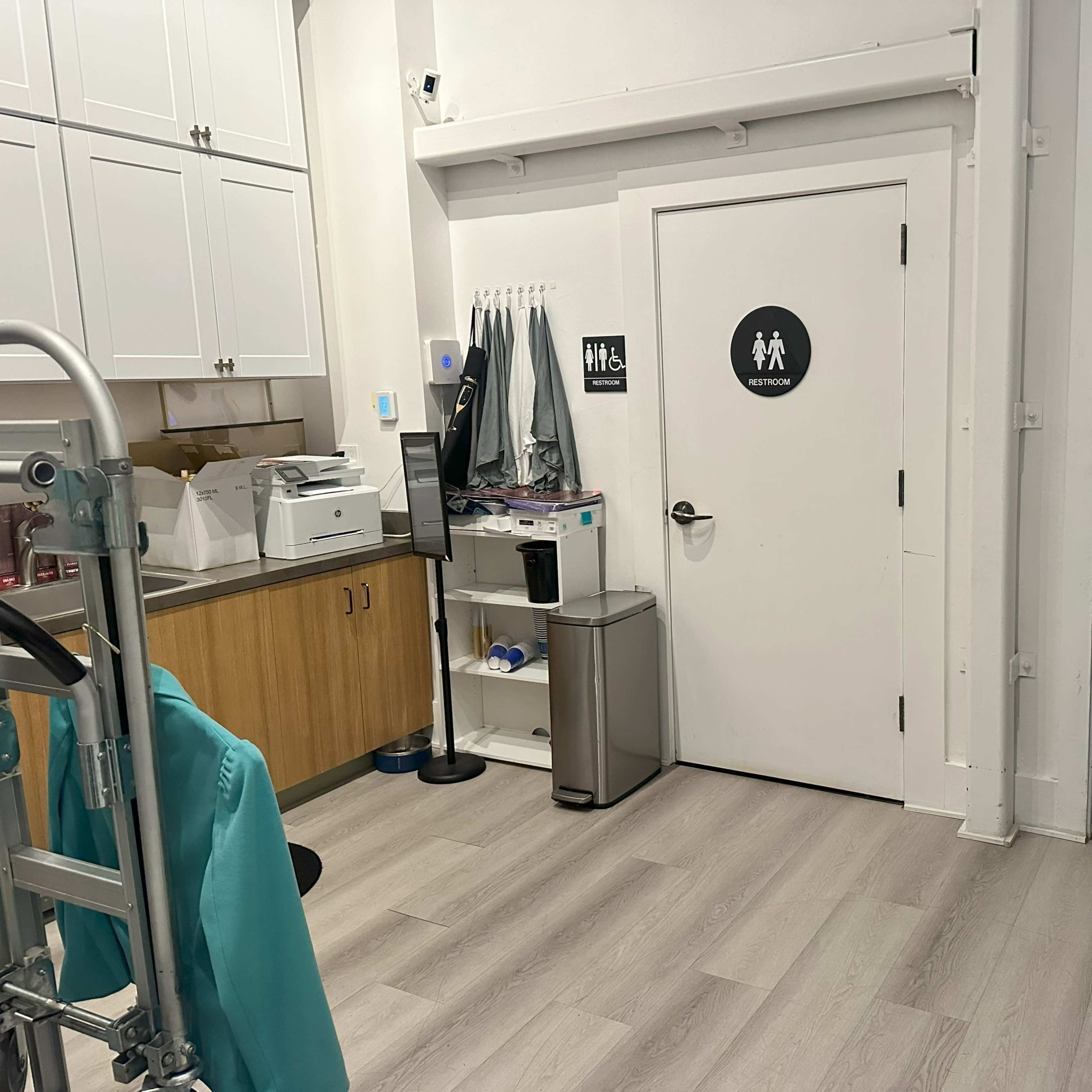 An interior space with a printer, trash can, and a door labeled for restroom access.