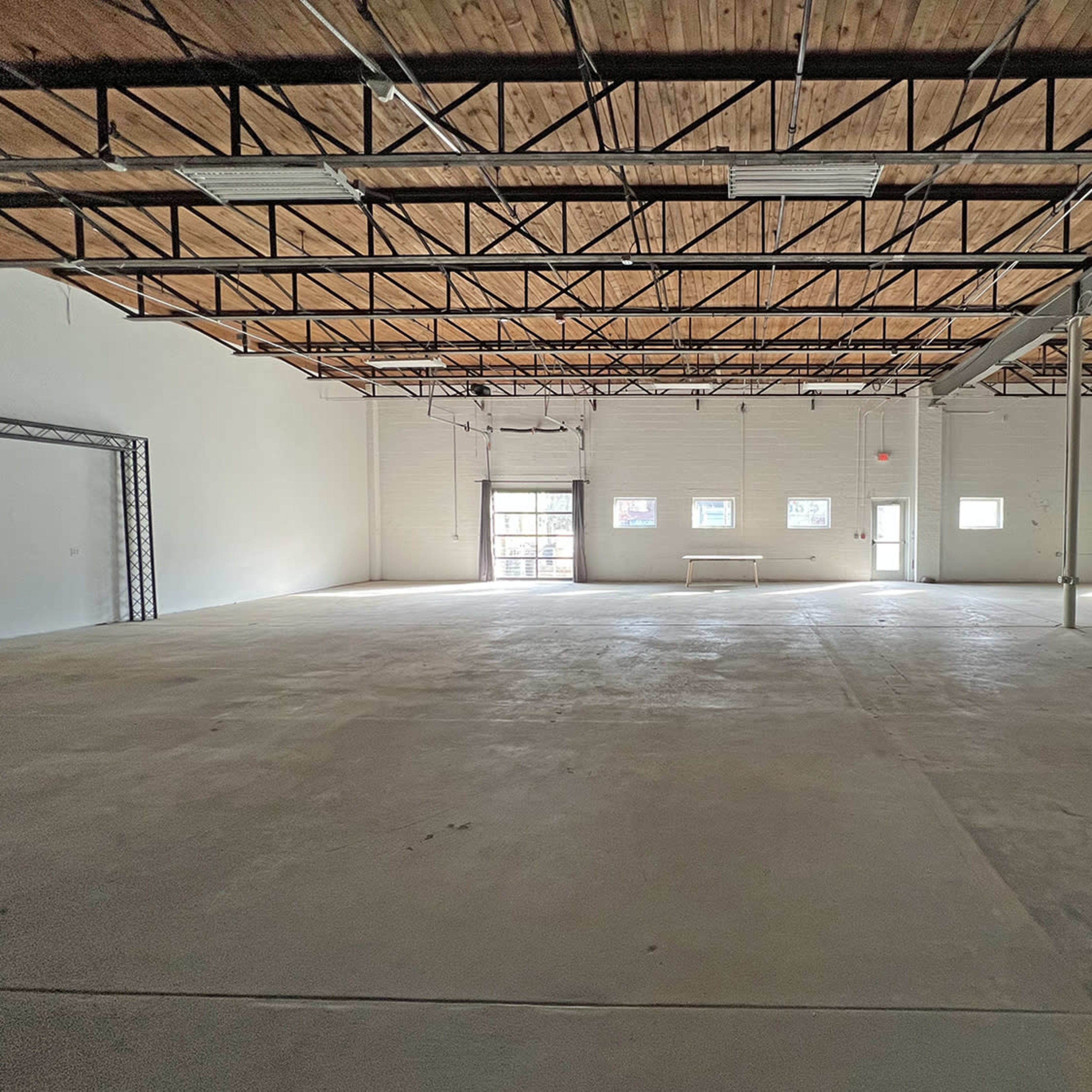 A large, empty warehouse space with a concrete floor and high, wooden-beamed ceilings.