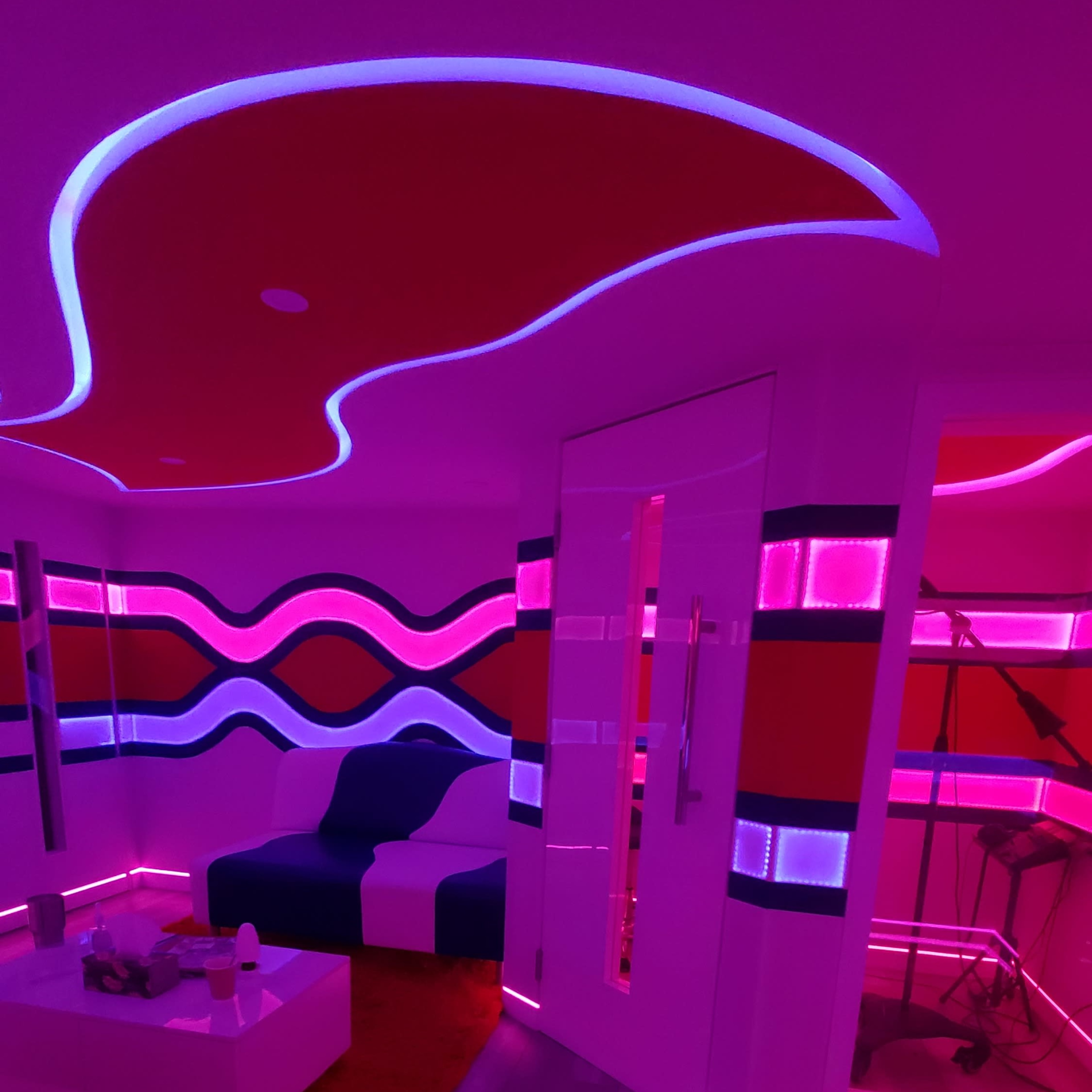 The room features modern furniture with curved lines and vibrant purple and red lighting accents.