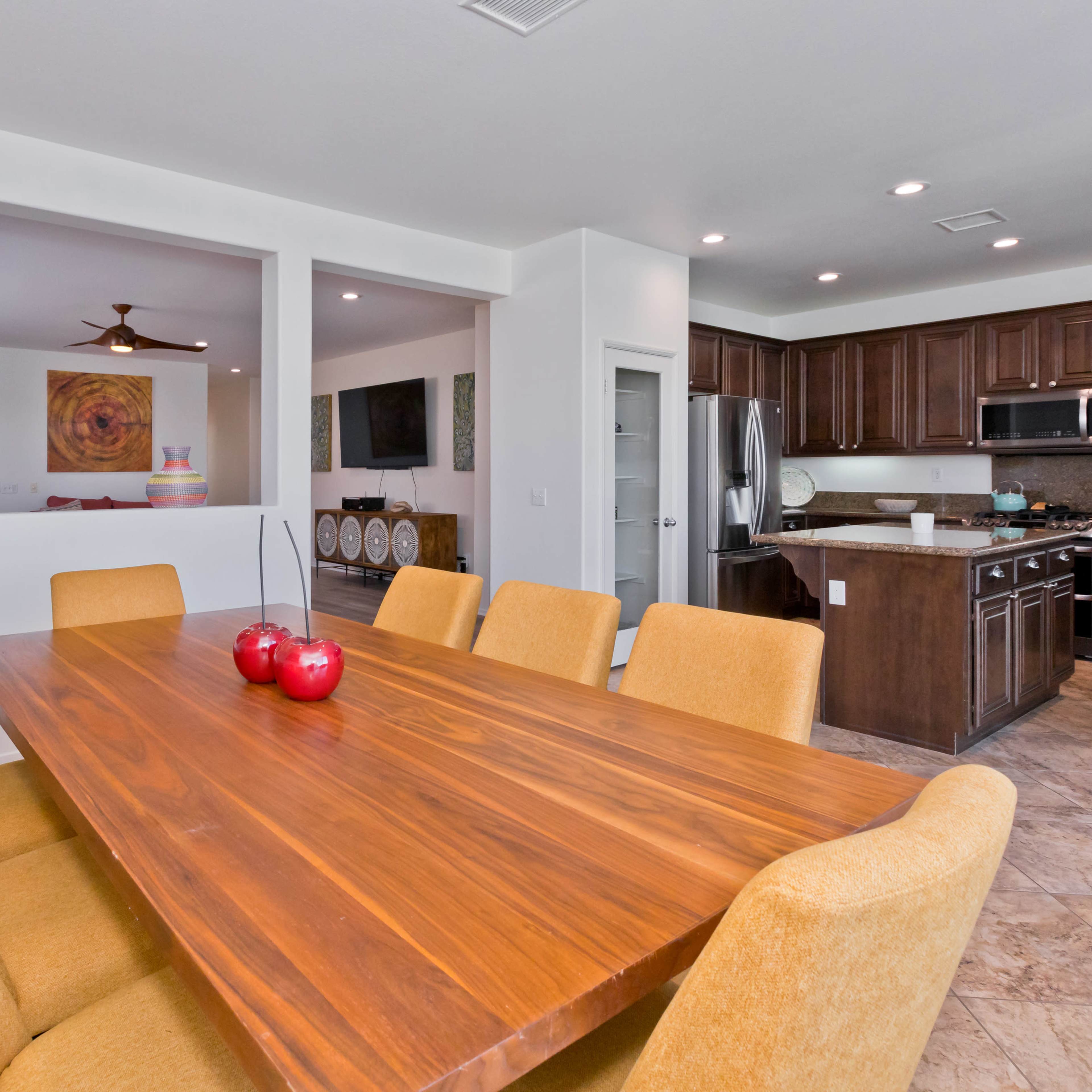 A spacious dining area features a large wooden table surrounded by yellow upholstered chairs, adjacent to an open kitchen with dark cabinetry.