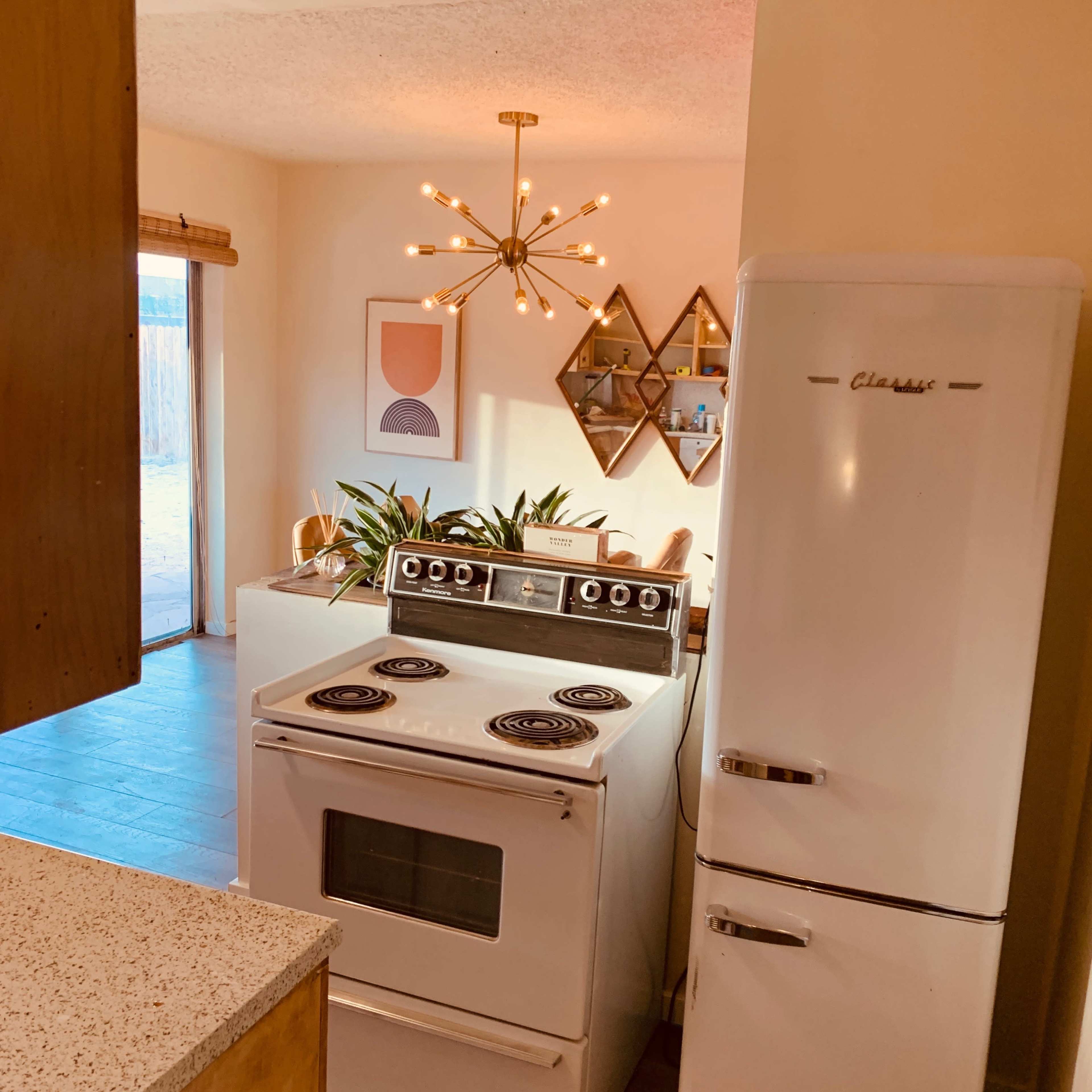 The kitchen features a vintage white stove and refrigerator, with a modern light fixture above and decorative plants on the countertop.