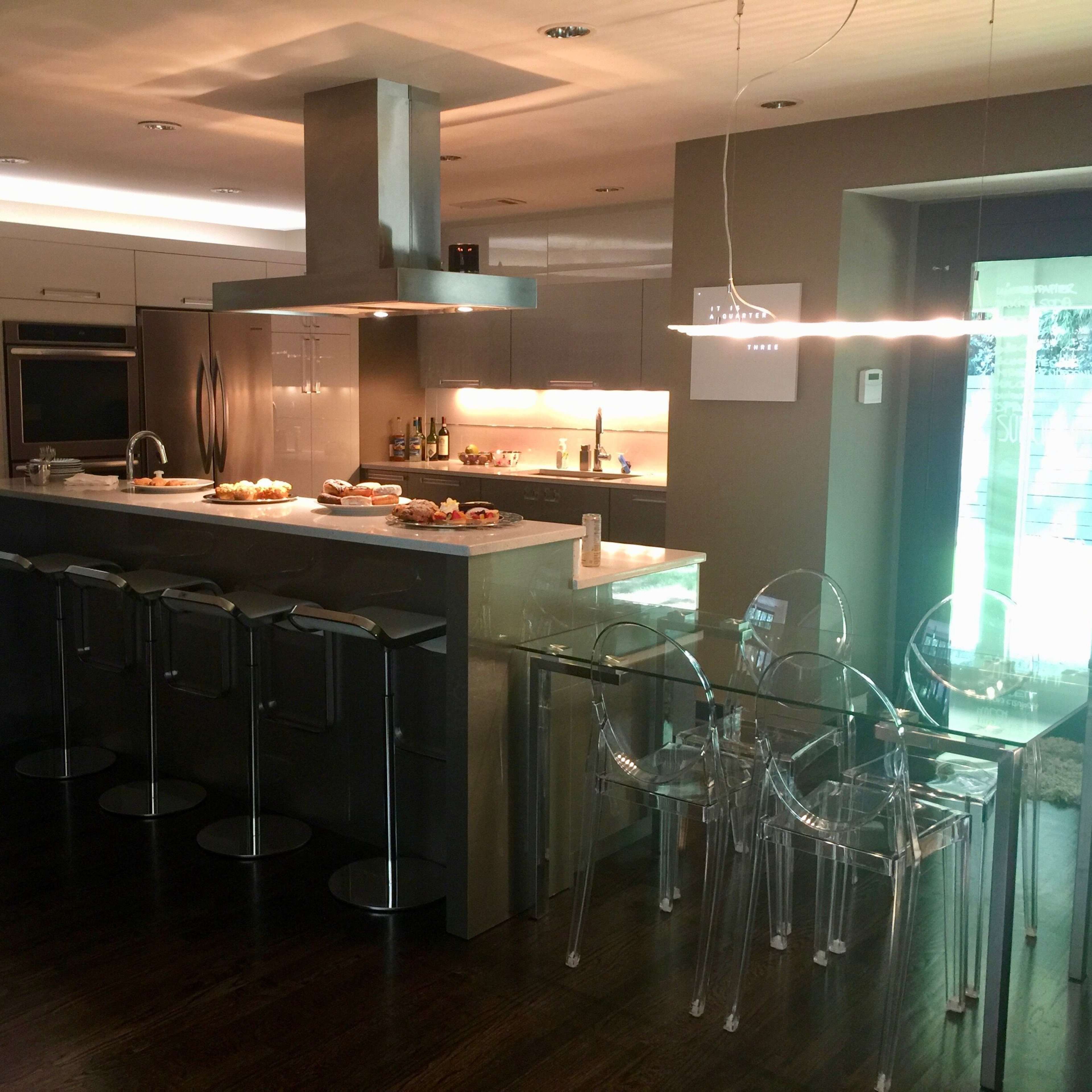 A modern kitchen with a large island, bar stools, and a dining area featuring clear acrylic chairs.