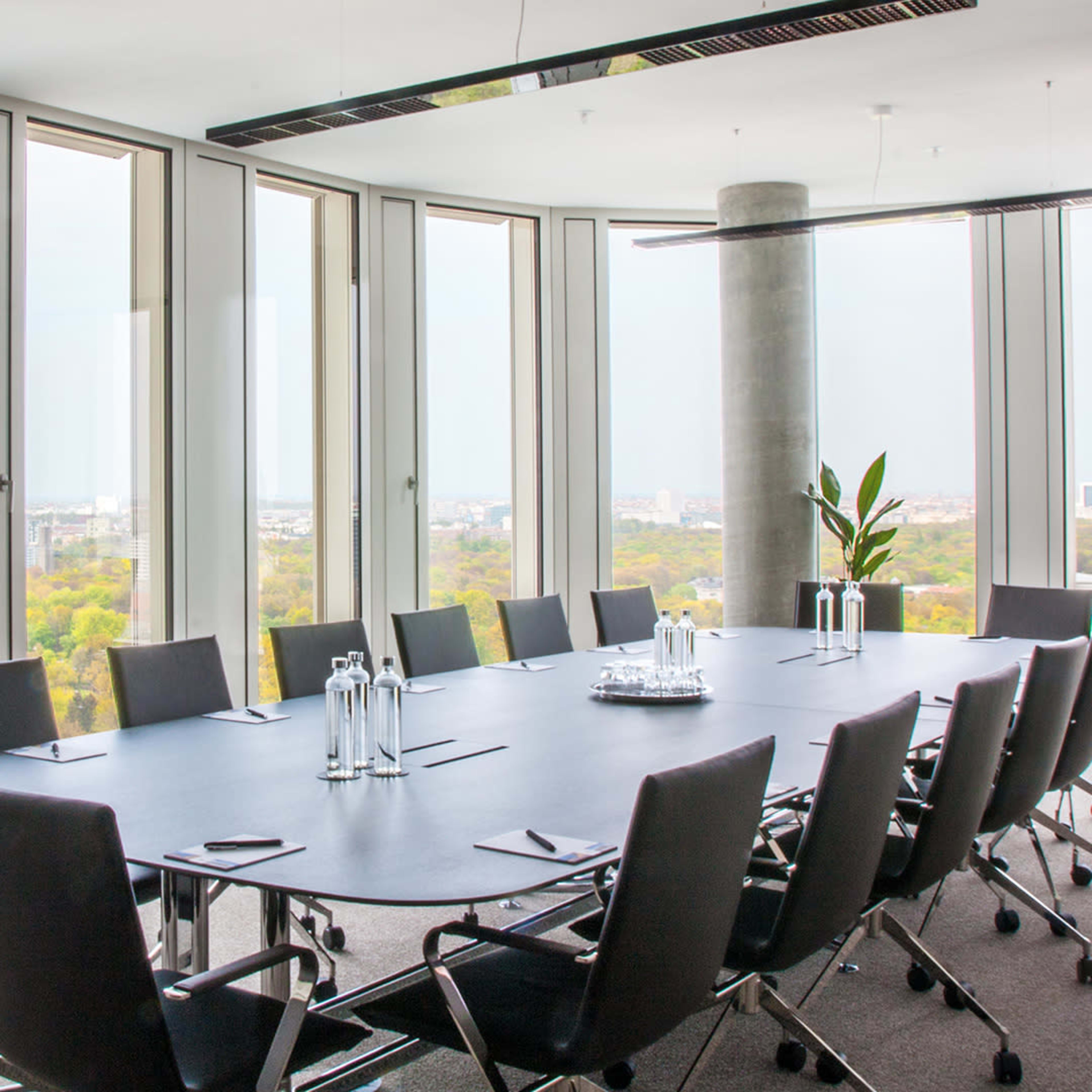 A modern conference room features a long black table surrounded by ergonomic chairs, with large windows offering a panoramic view of the city.