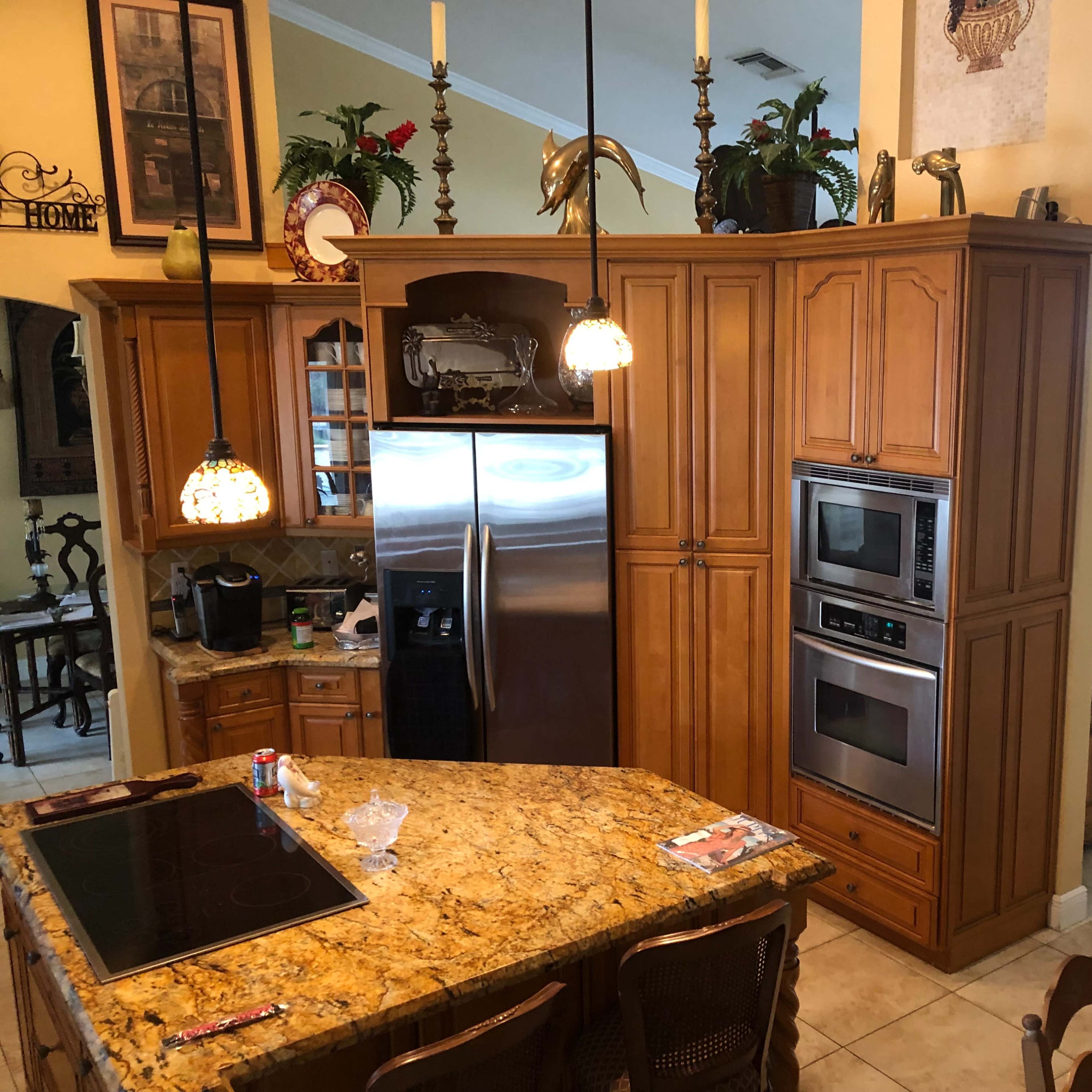 A spacious kitchen with wooden cabinetry, stainless steel appliances, and a countertop made of granite, adjoining a dining area and a hallway leading to another room.
