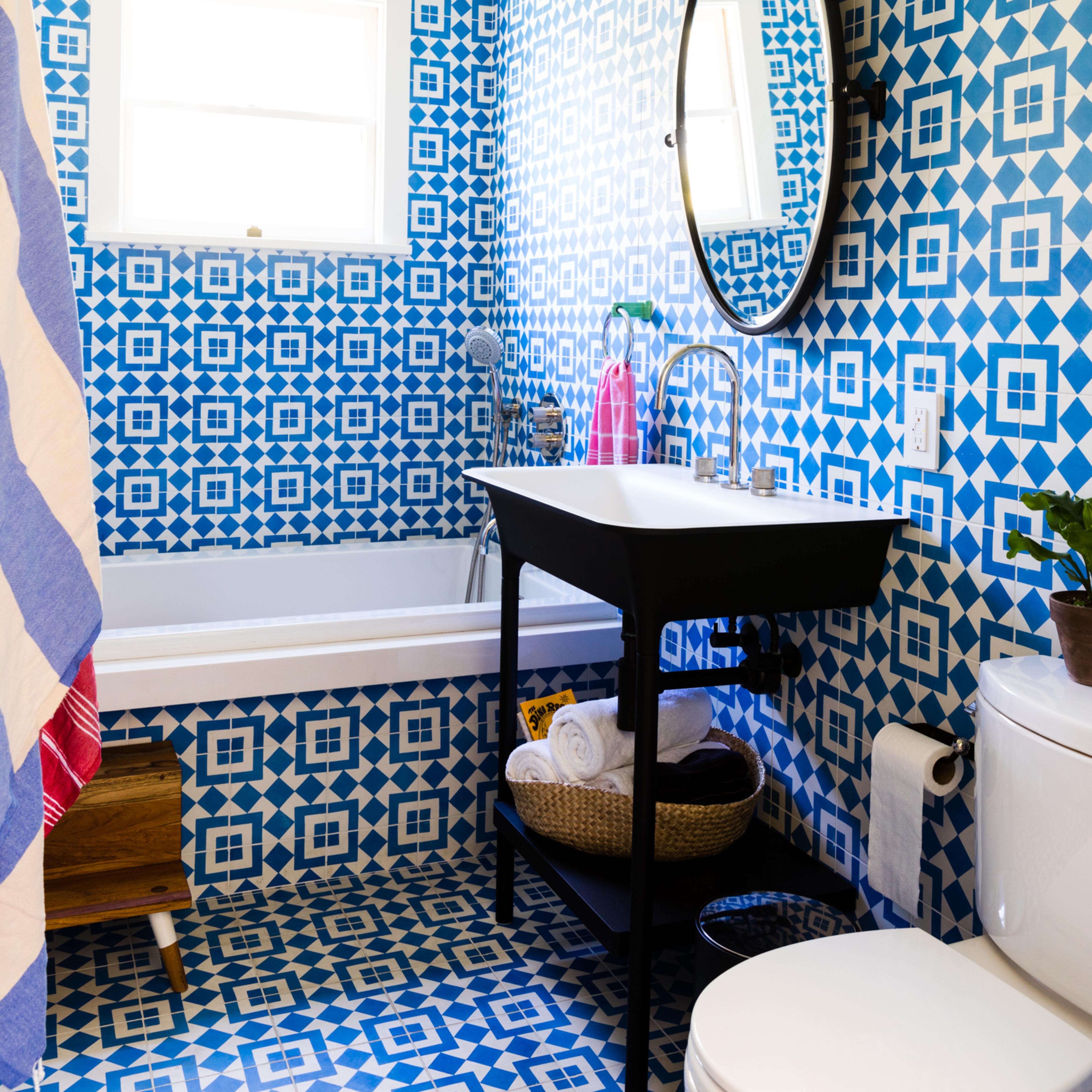 The bathroom features blue and white patterned walls and flooring, a freestanding black sink with a round mirror, and a bathtub under a window.