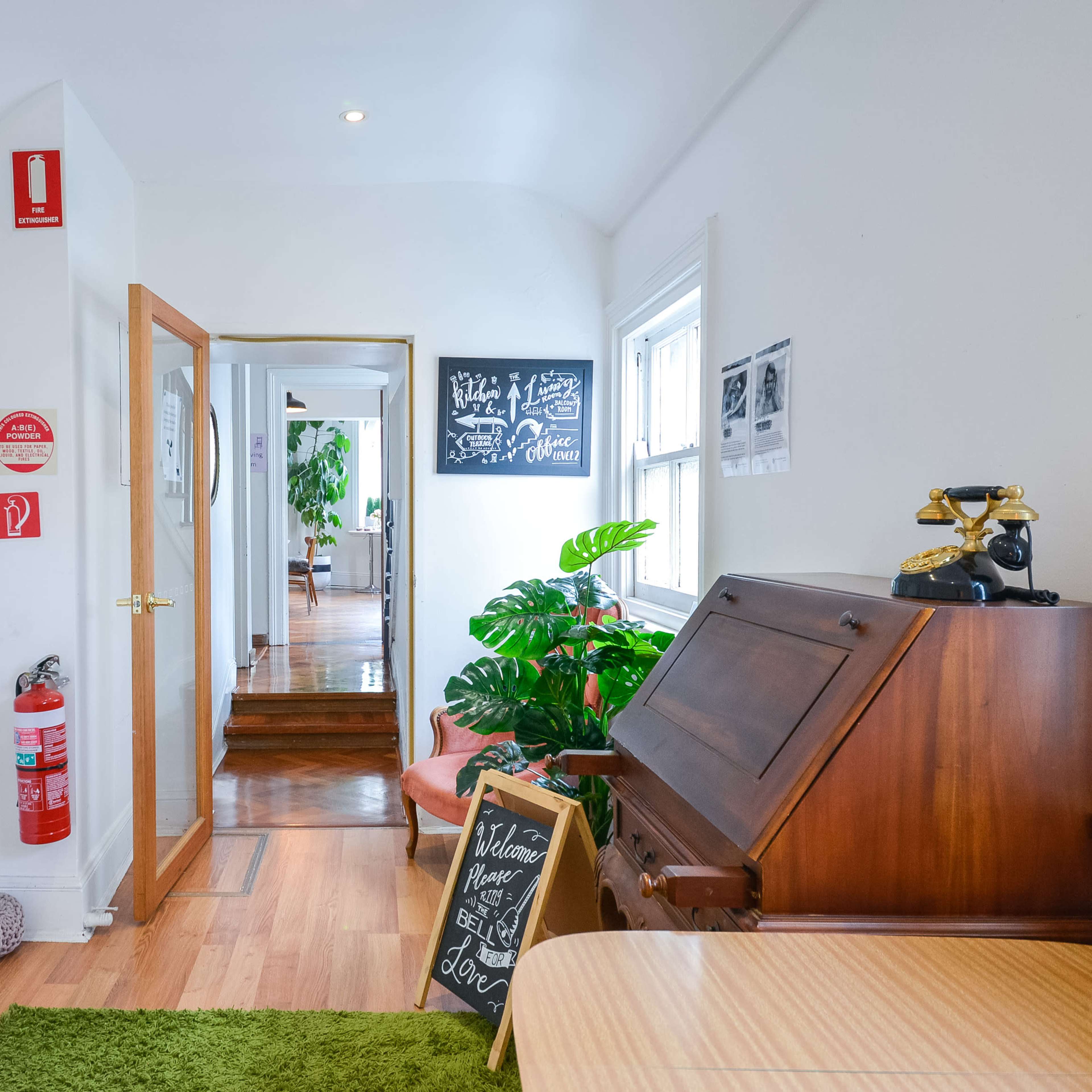 A hallway features a wooden desk, green plants, and signs indicating various rooms.