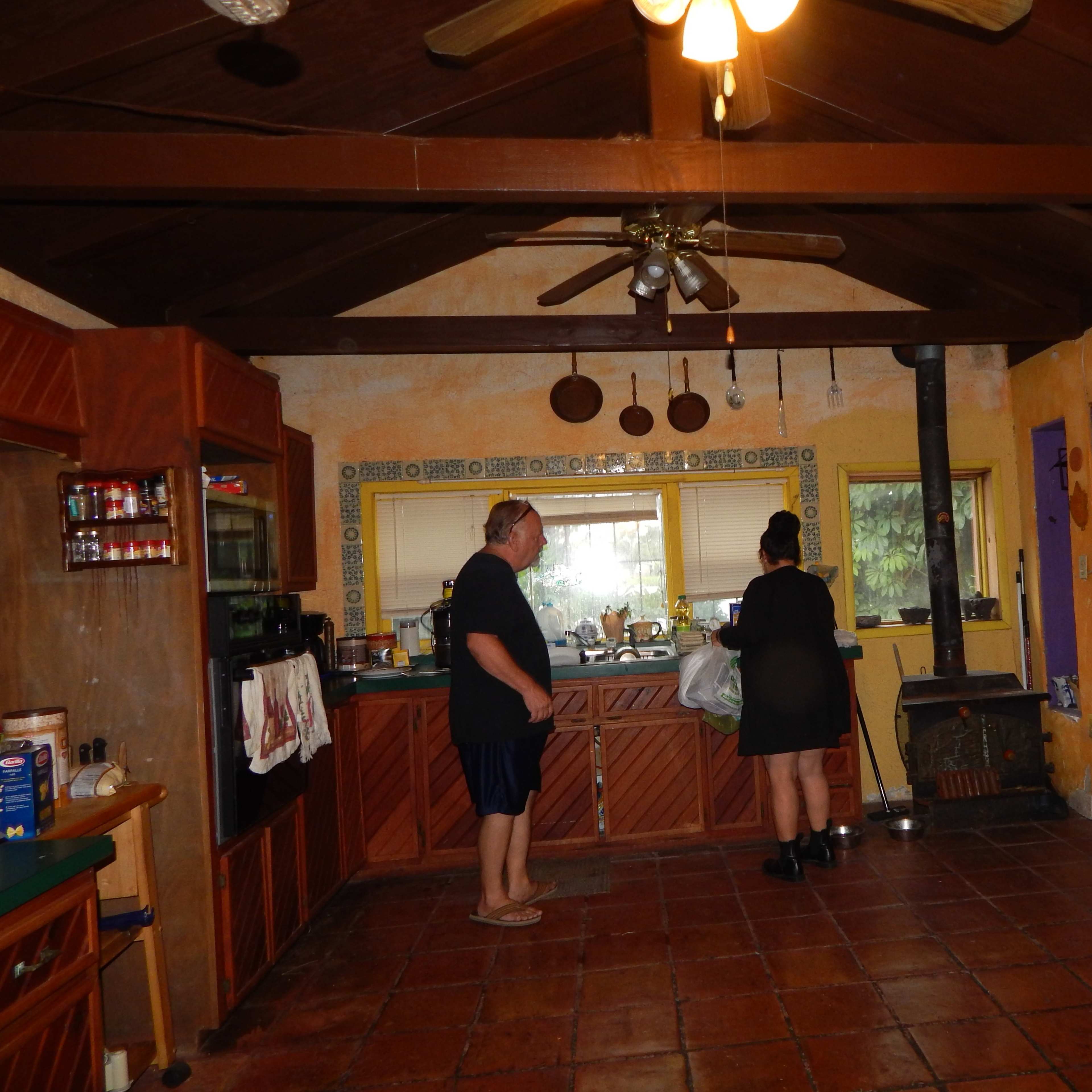 A group of three people is working in a spacious kitchen with wooden cabinets and a high, beamed ceiling.
