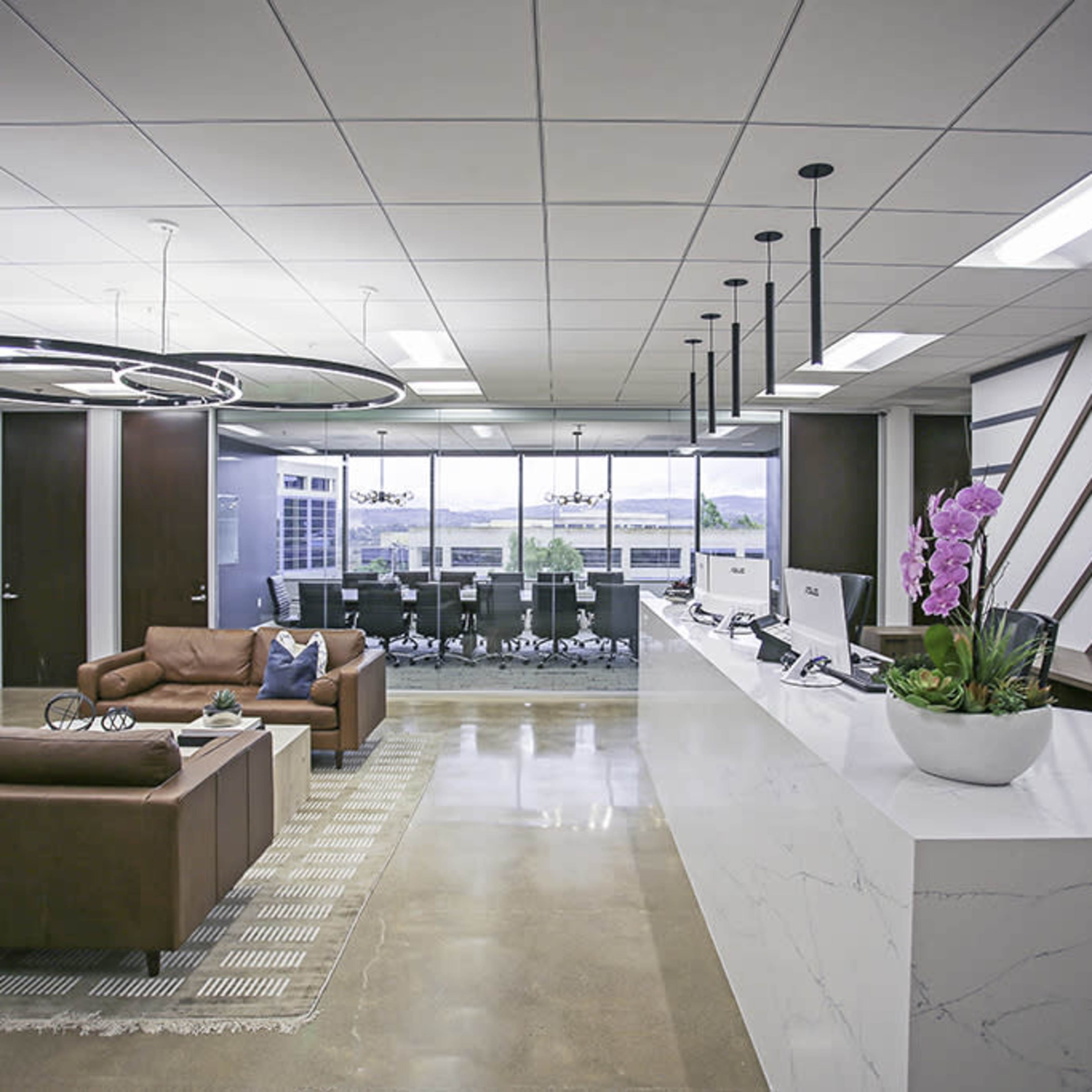 A modern office reception area with a white marble counter, a seating area with a brown couch, and a large glass meeting room in the background.
