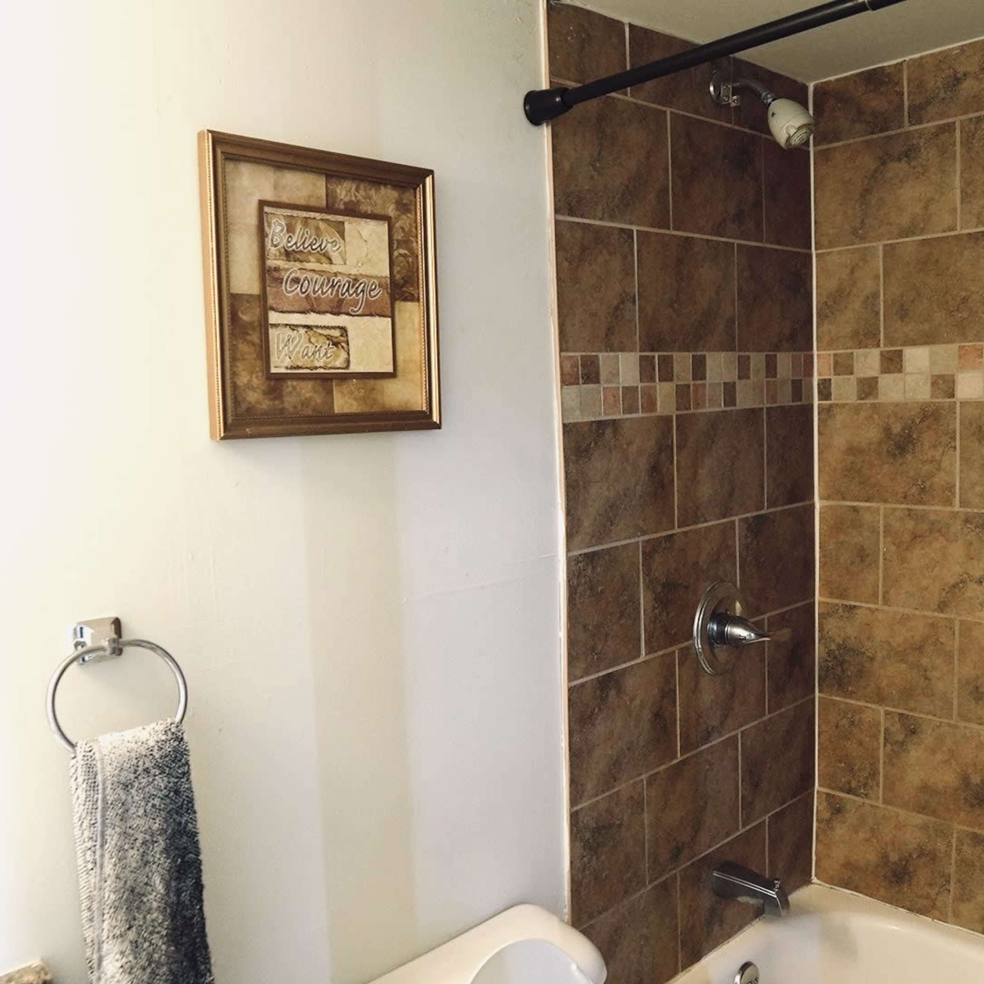 A bathroom with a tiled shower area, a framed wall decoration, and a towel hanging on a rack.