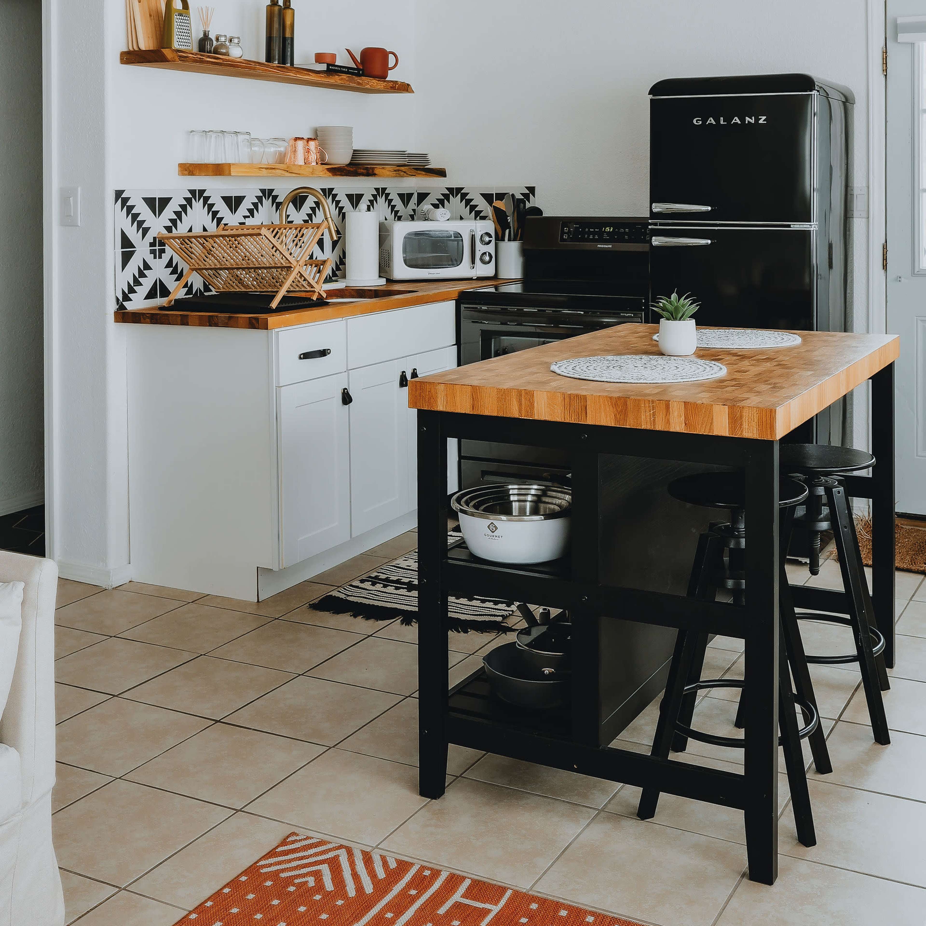 A modern kitchen with a black refrigerator, wooden countertops, open shelving, and a dining table with black stools.