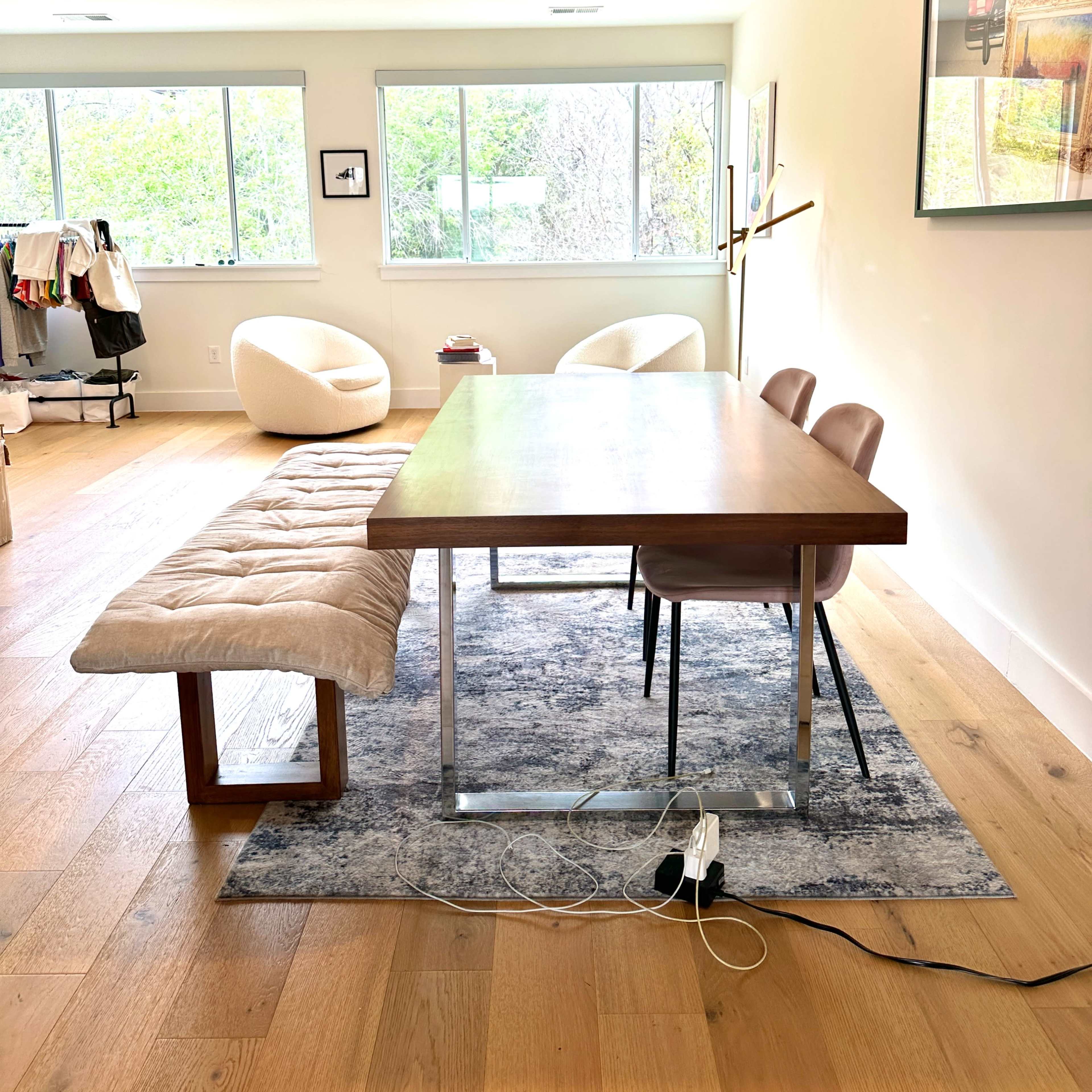 A modern dining area features a wooden table with a bench and two chairs on a patterned rug, surrounded by large windows.