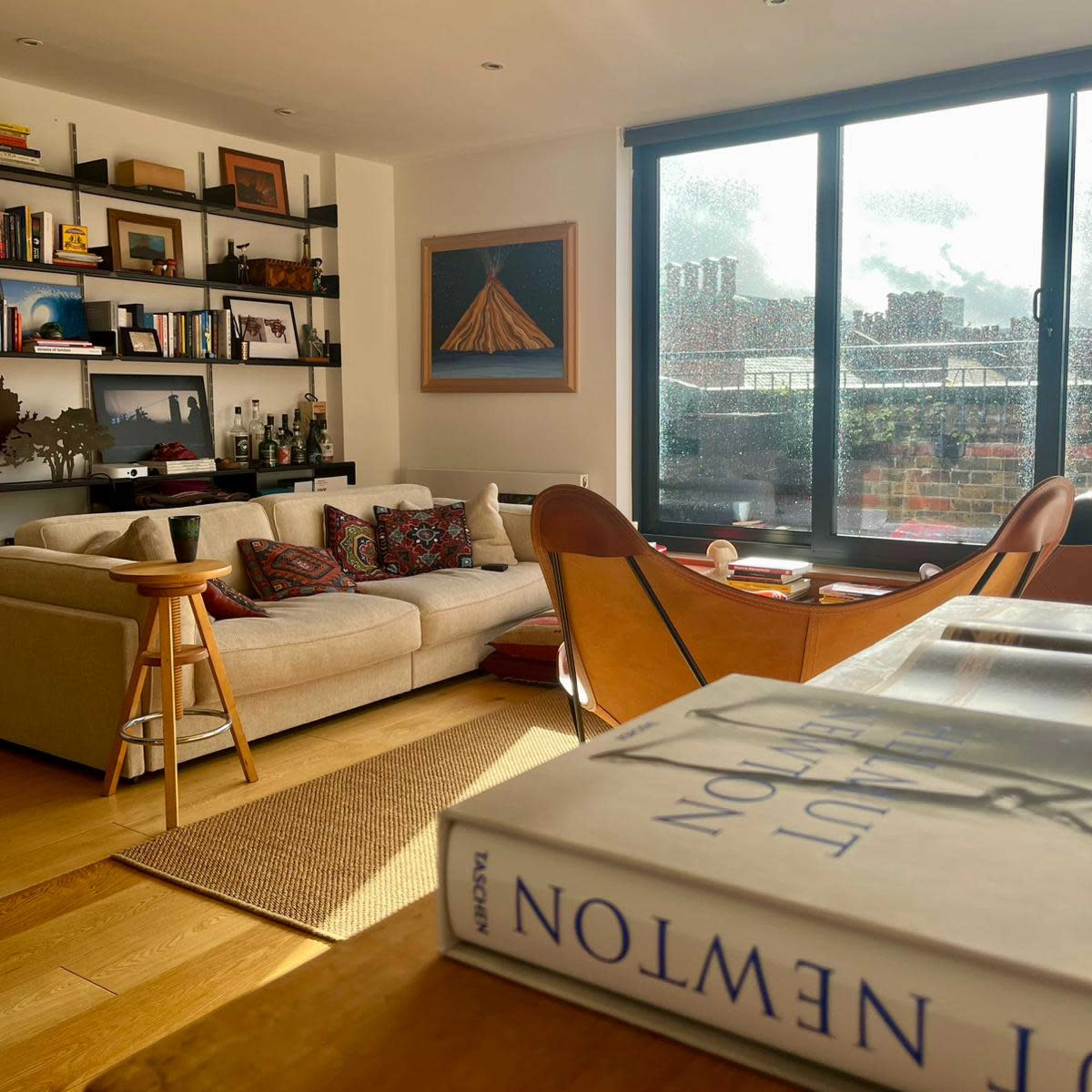 A cozy living room features a beige sofa, wooden shelves filled with books, and a coffee table with a book lying open.