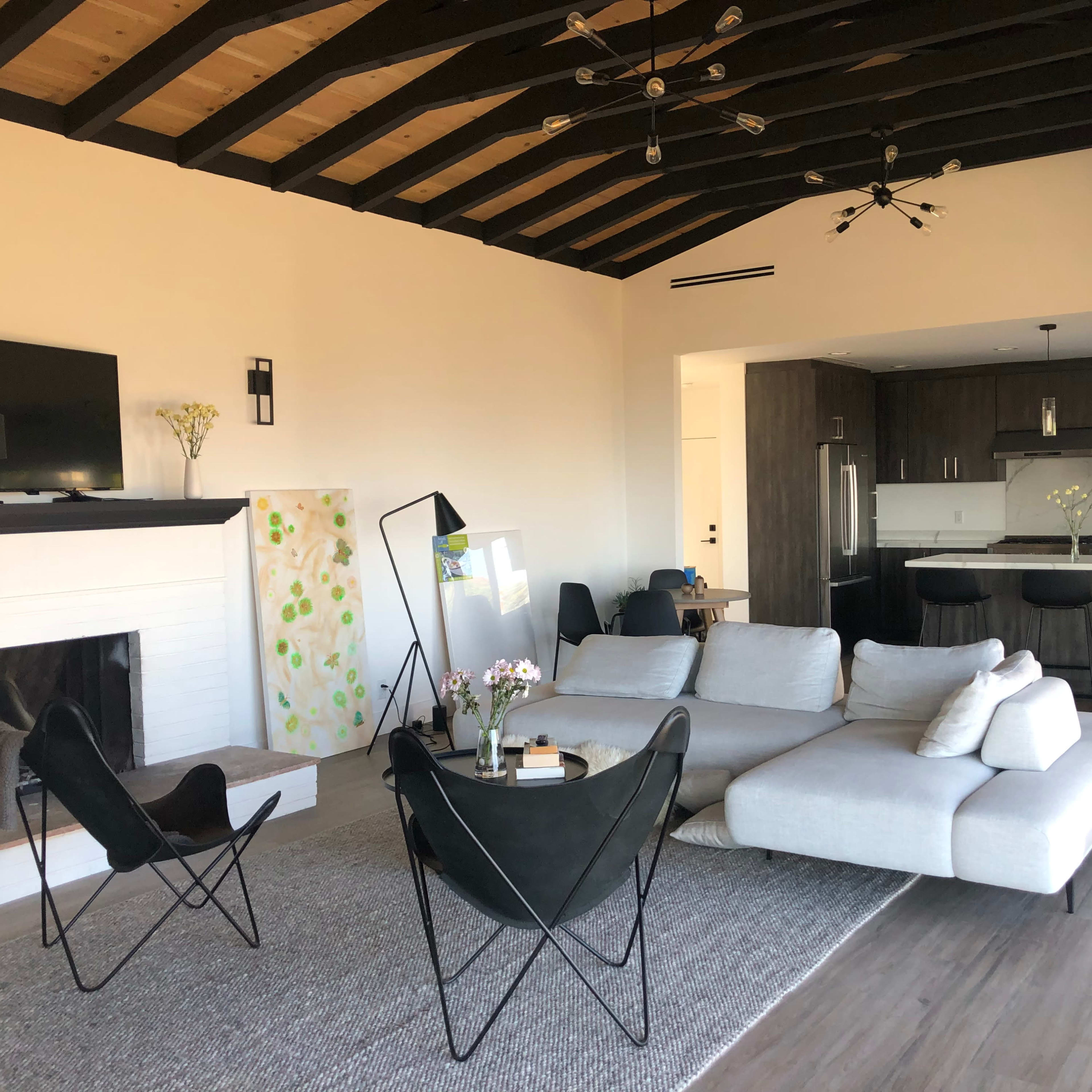 A modern living room with a sectional sofa, a black chair, a coffee table, a fireplace, and an open kitchen in the background.