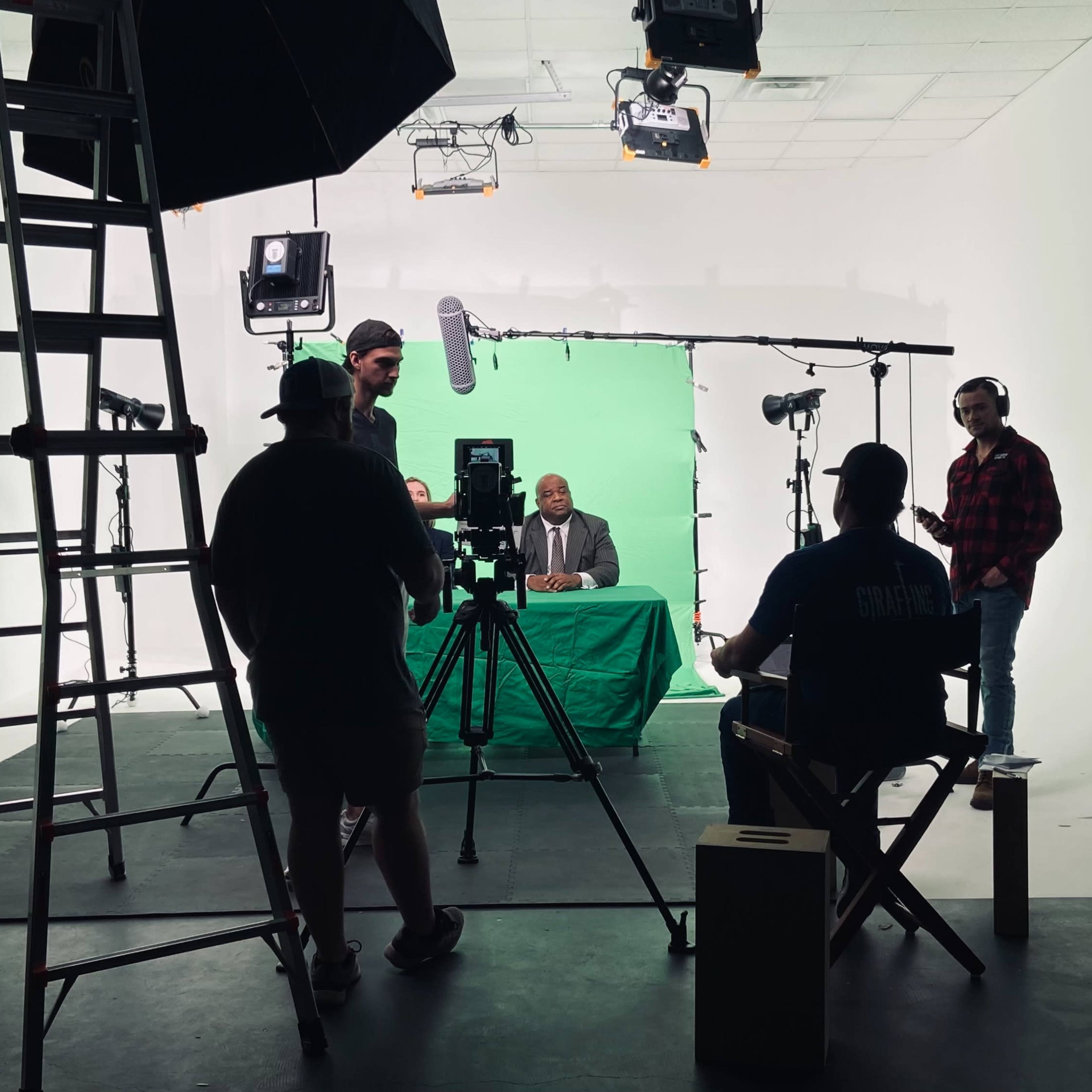 A film crew sets up for a recording session in a studio with a green screen backdrop.