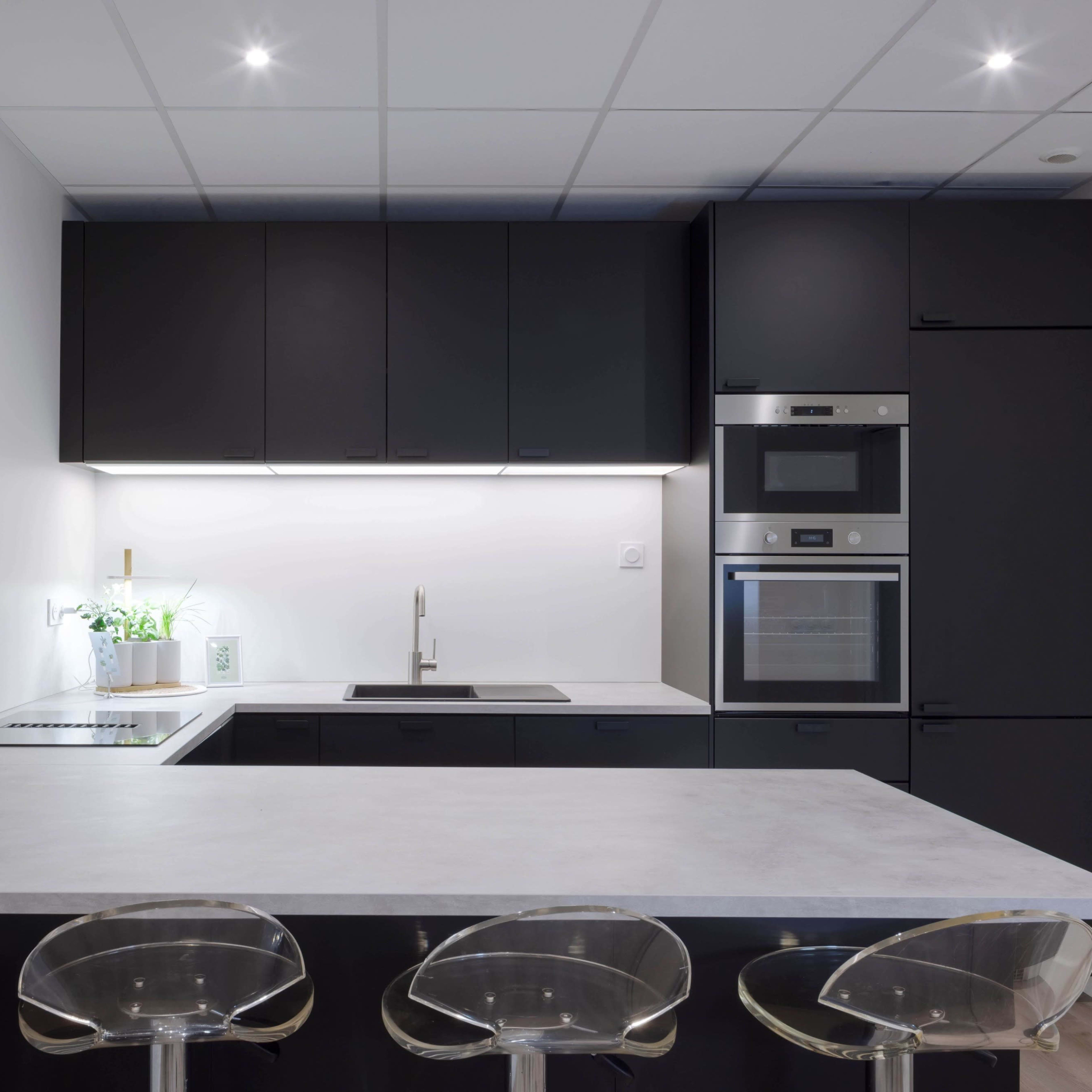 A modern kitchen with black cabinetry, a white countertop, and three transparent stools at a kitchen island.