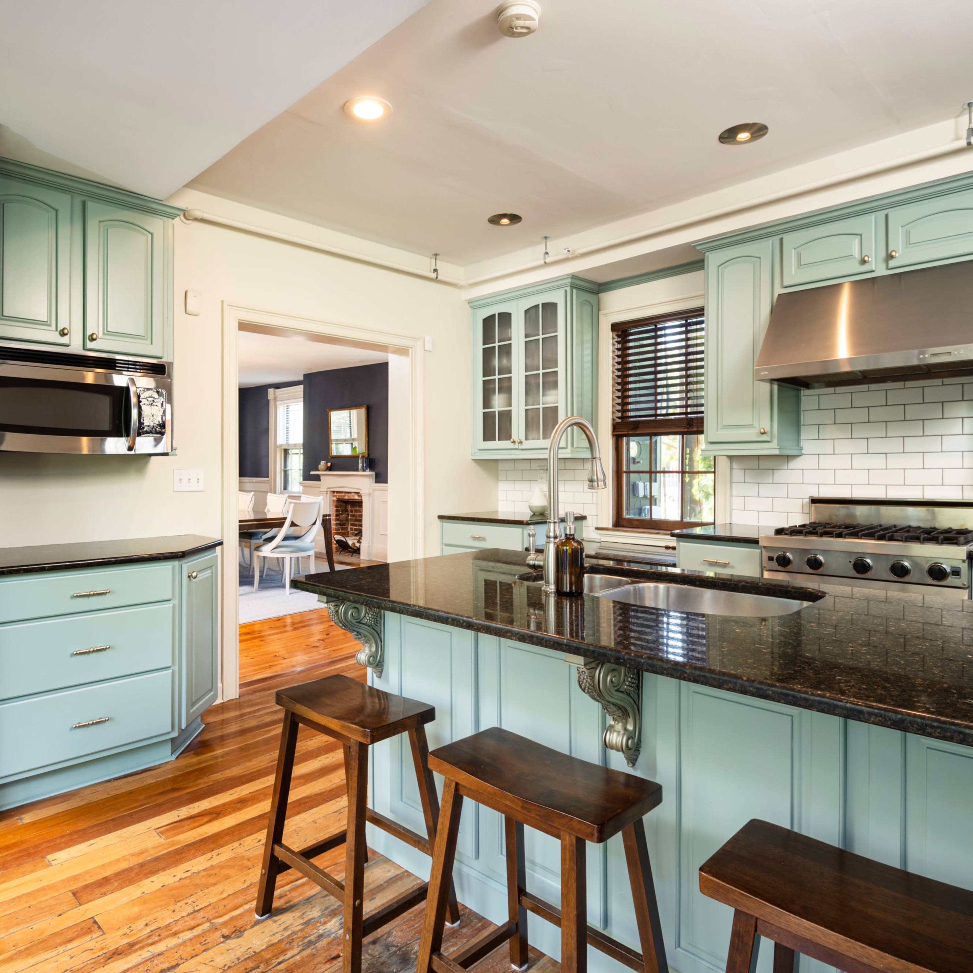A modern kitchen with mint green cabinets, a stainless steel refrigerator, and a black granite countertop with wooden bar stools.