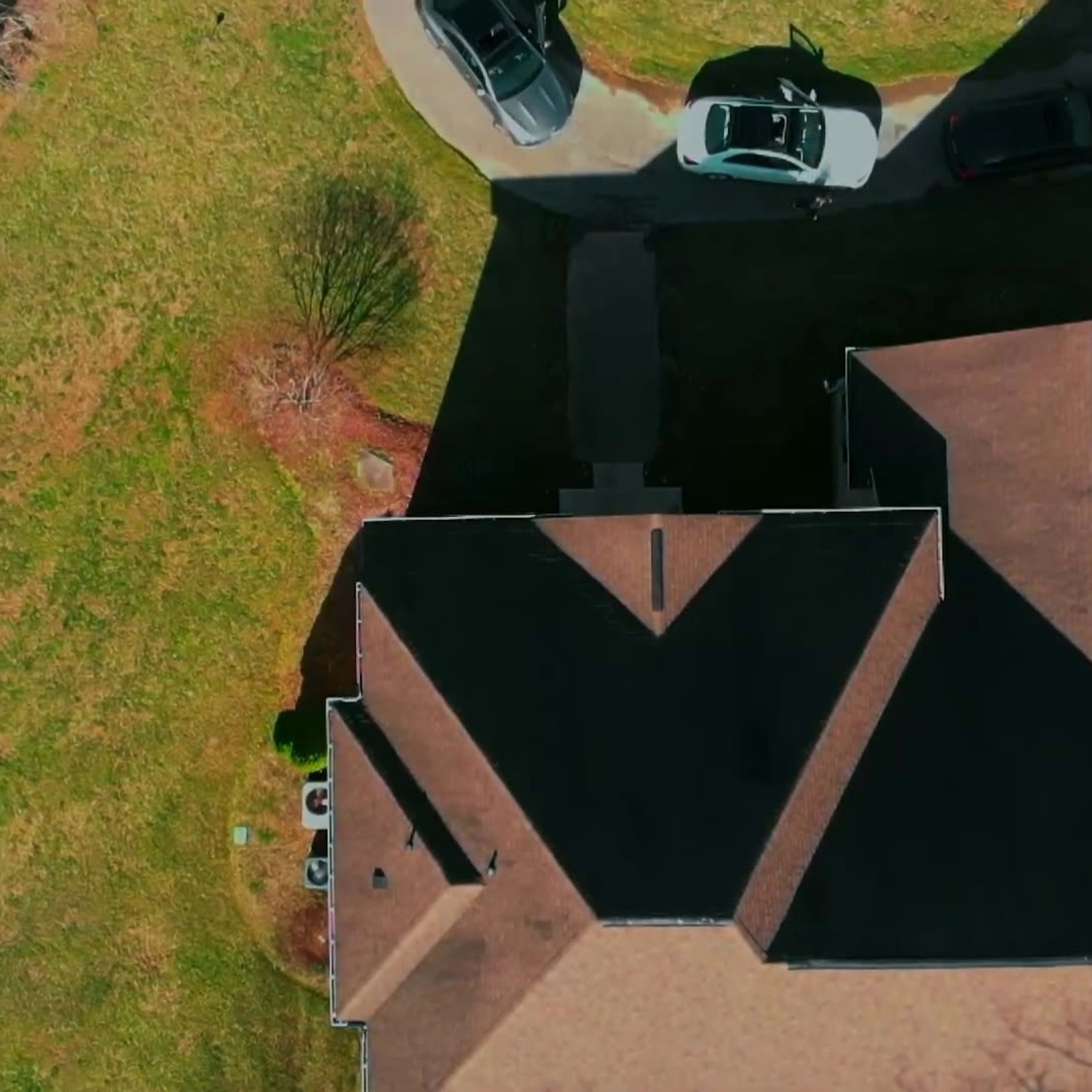 An aerial view of a residential property with several cars parked in a driveway and a large expanse of grass surrounding the house.