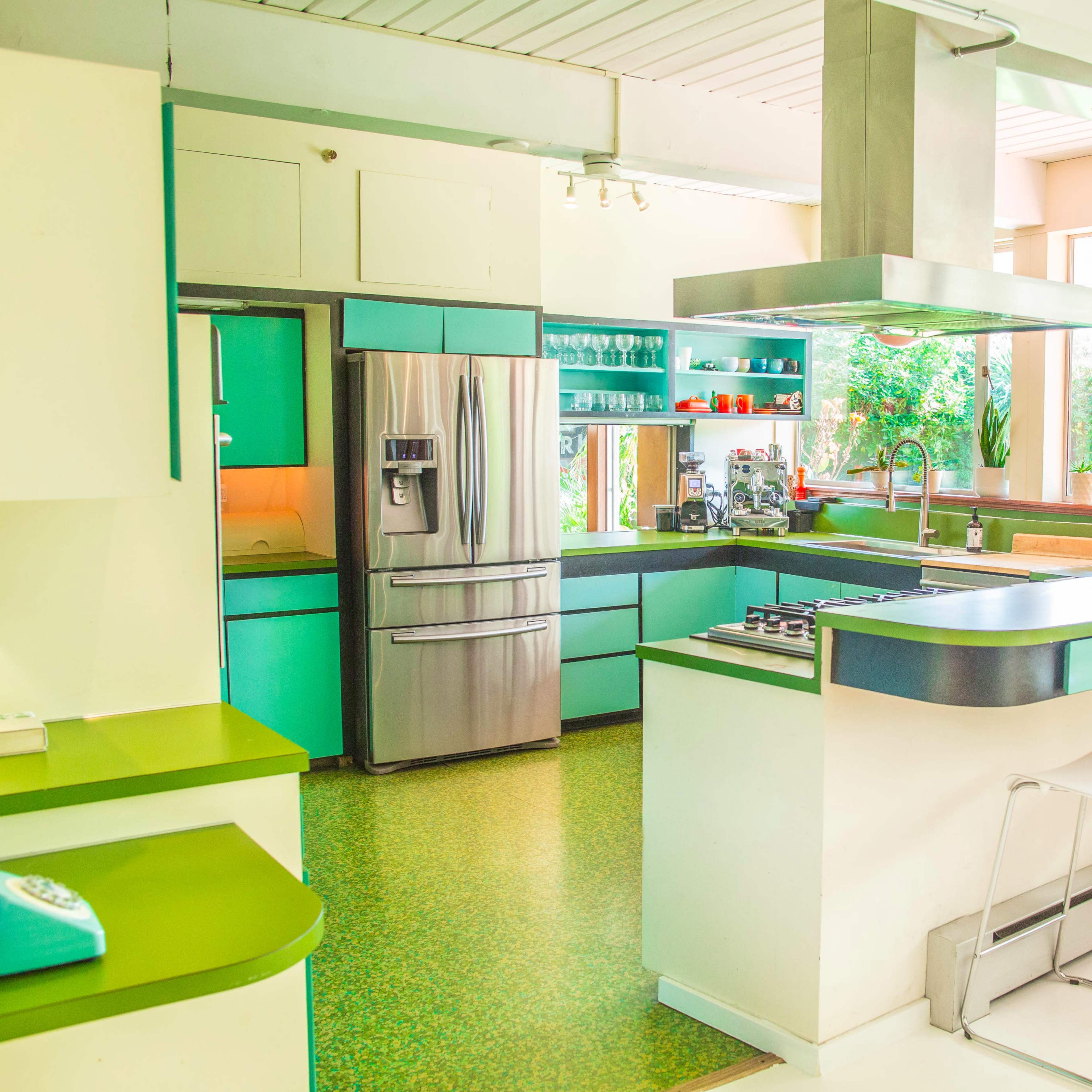 A modern kitchen features green and white cabinetry, stainless steel appliances, and a central island with bar stools.