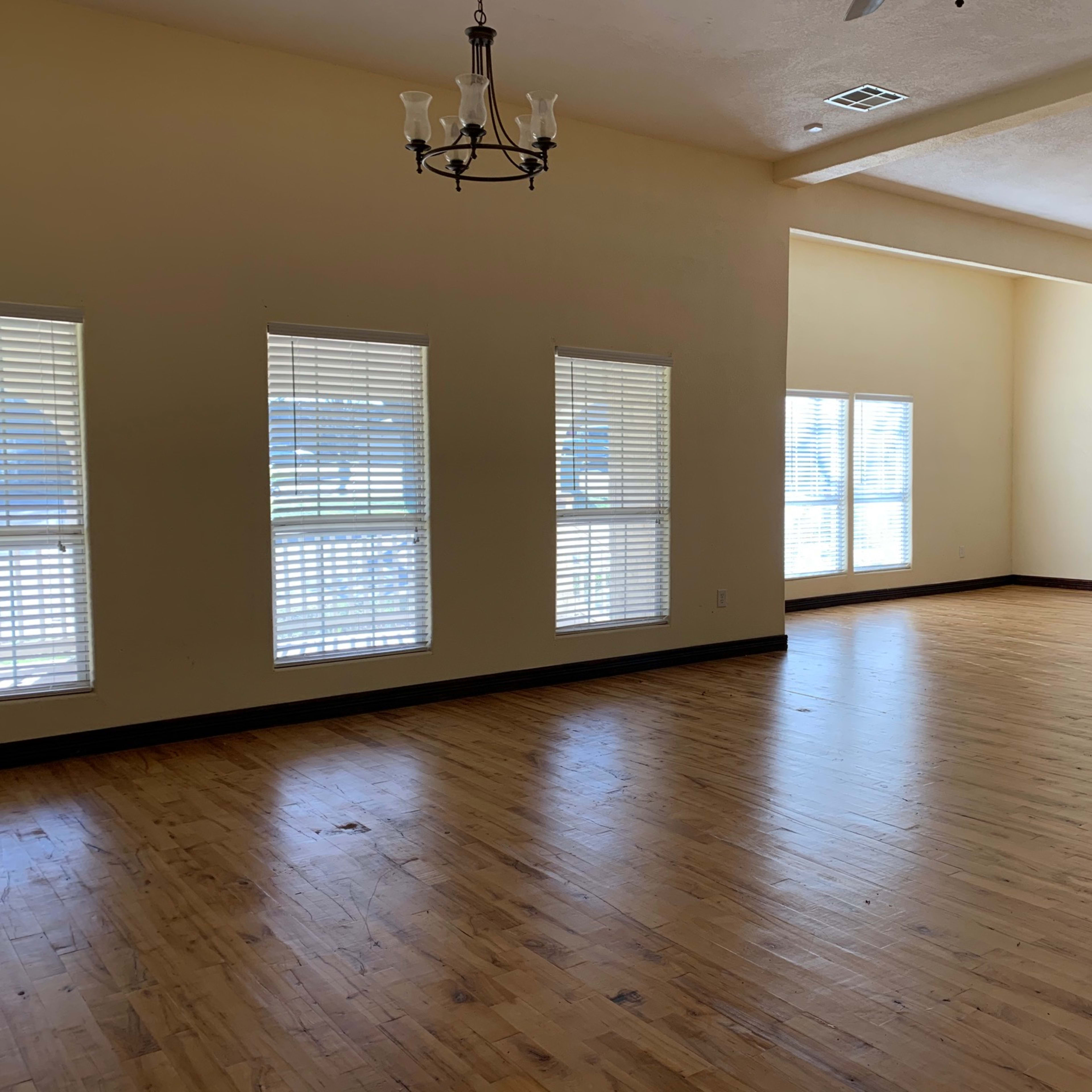 A spacious room with wooden flooring, large windows, and two ceiling fans.