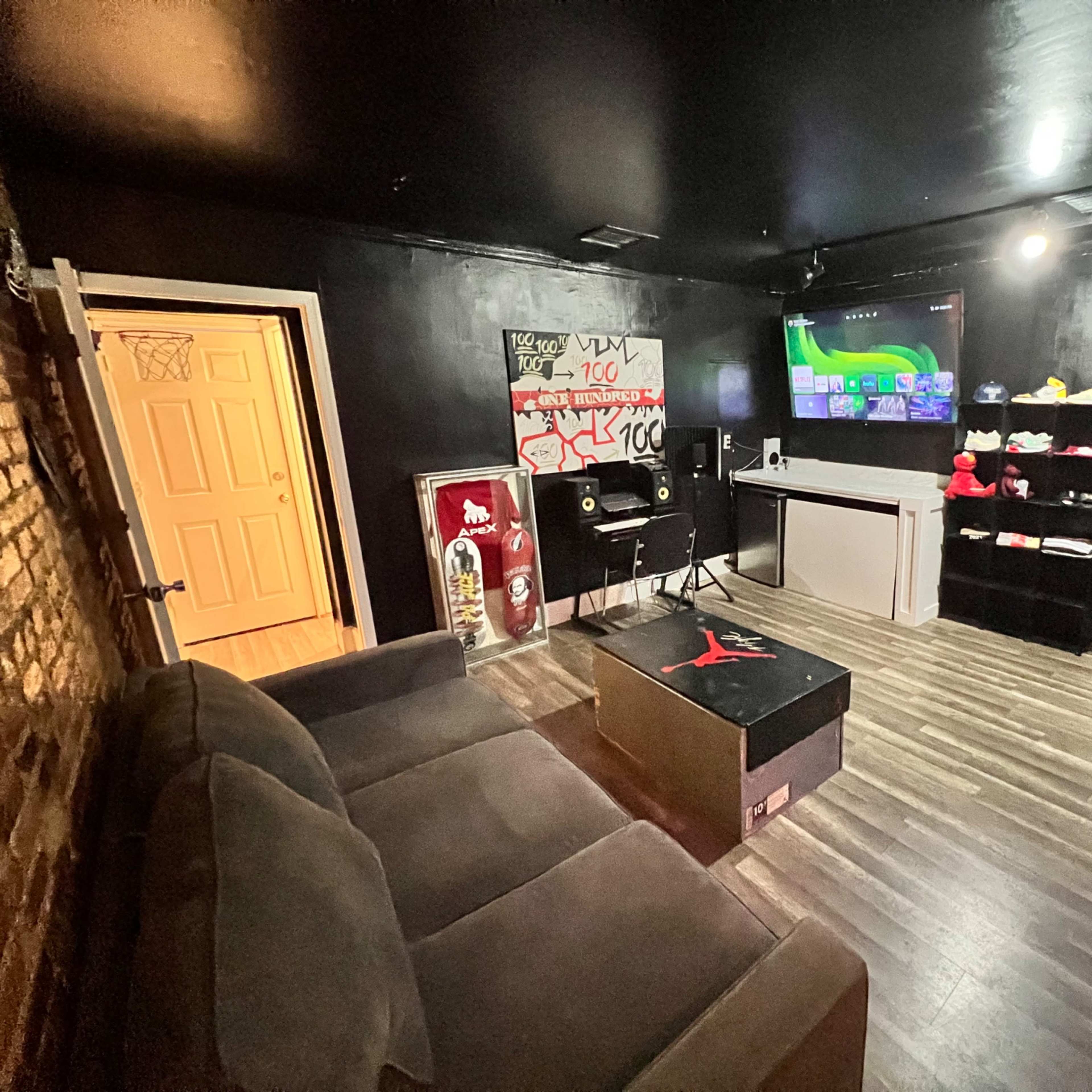 A small room features a dark-colored couch, a coffee table with a graphic design, audio equipment, and shelves displaying shoes and accessories.