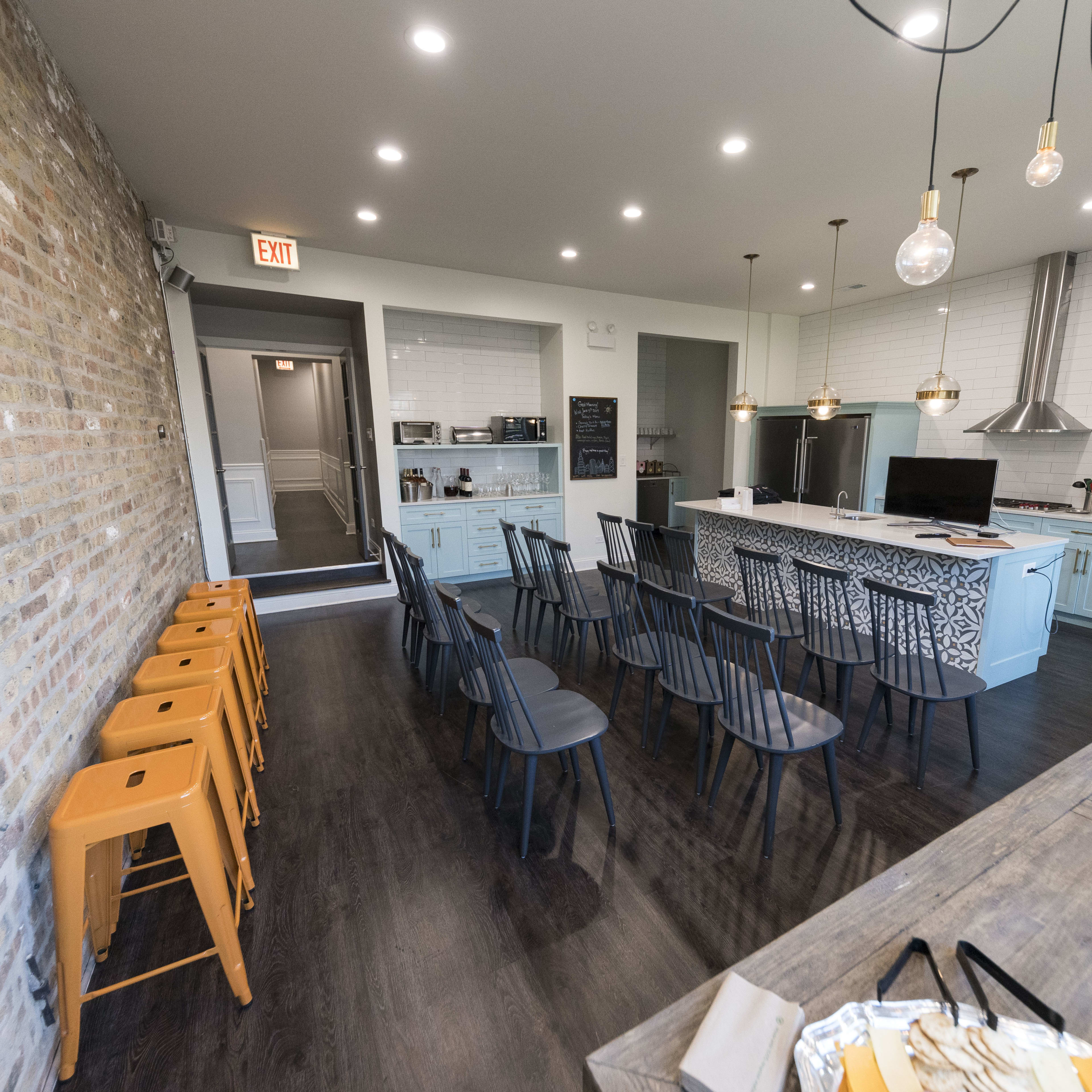 A modern kitchen and dining area with a seating arrangement of black chairs and orange barstools, featuring a brick wall and a well-equipped kitchen setup.