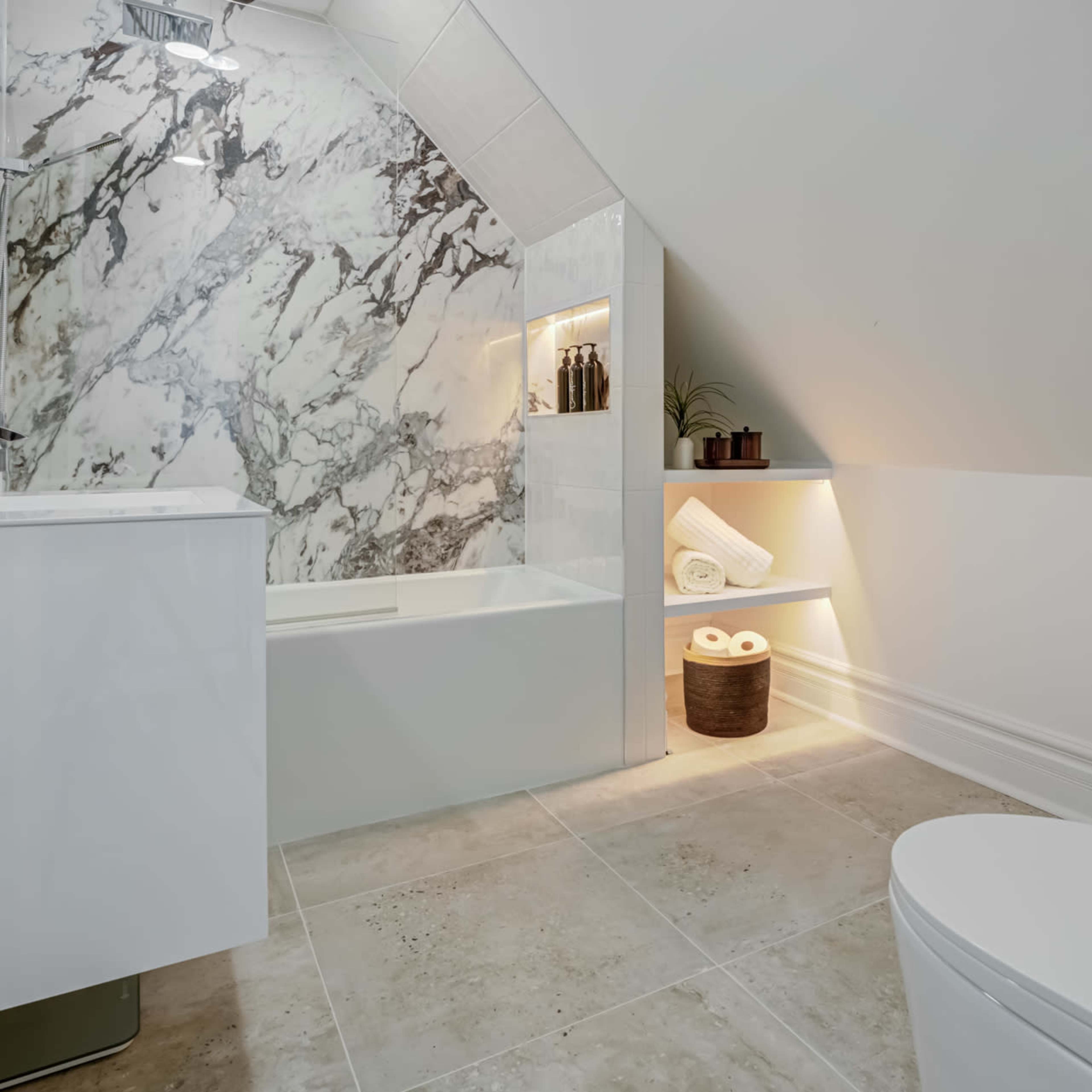 A modern bathroom with a marble accent wall, a bathtub, a toilet, and shelves displaying rolled towels.