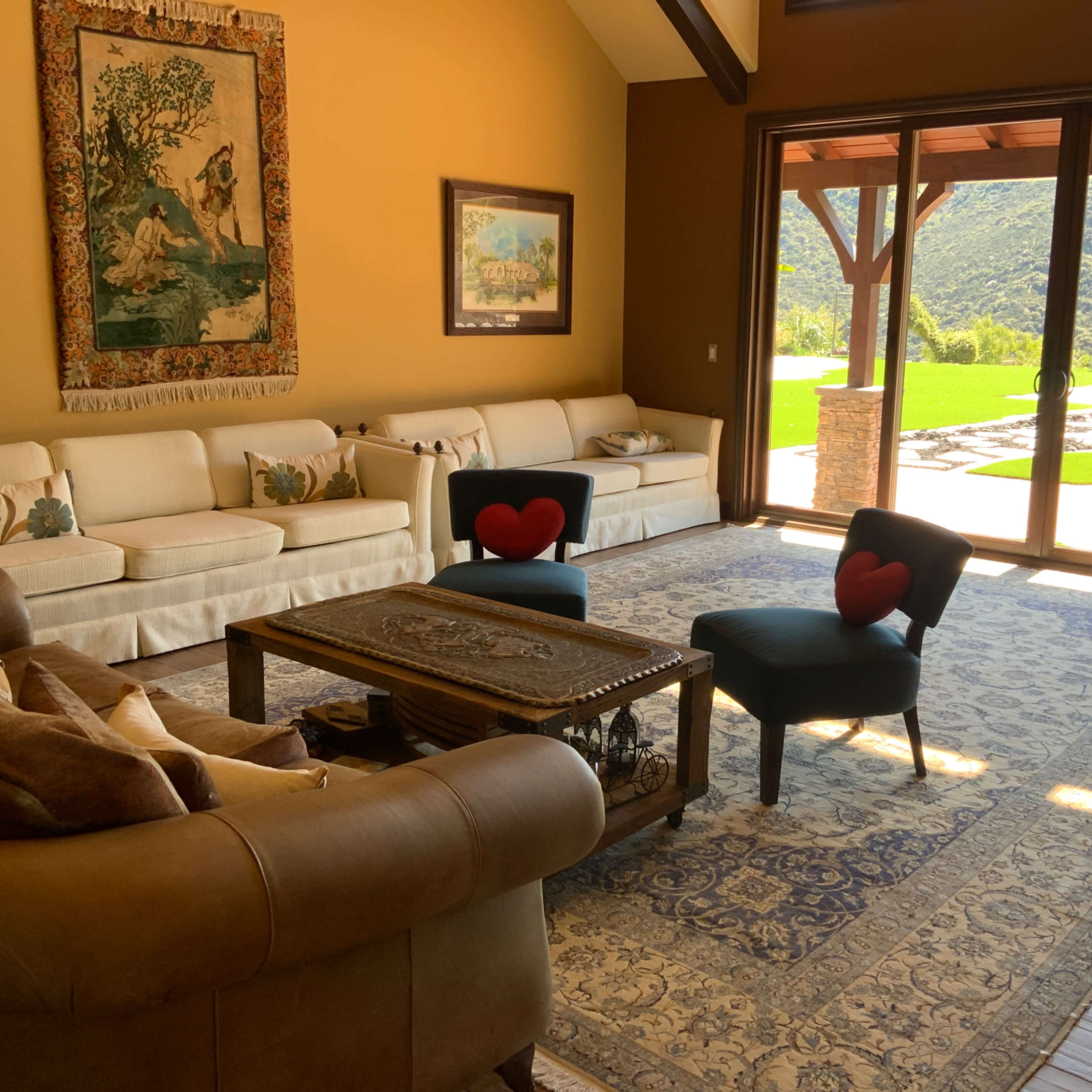 A spacious living room with a large window overlooking a patio and landscaped garden, featuring a mix of furniture arrangements and decorative elements.
