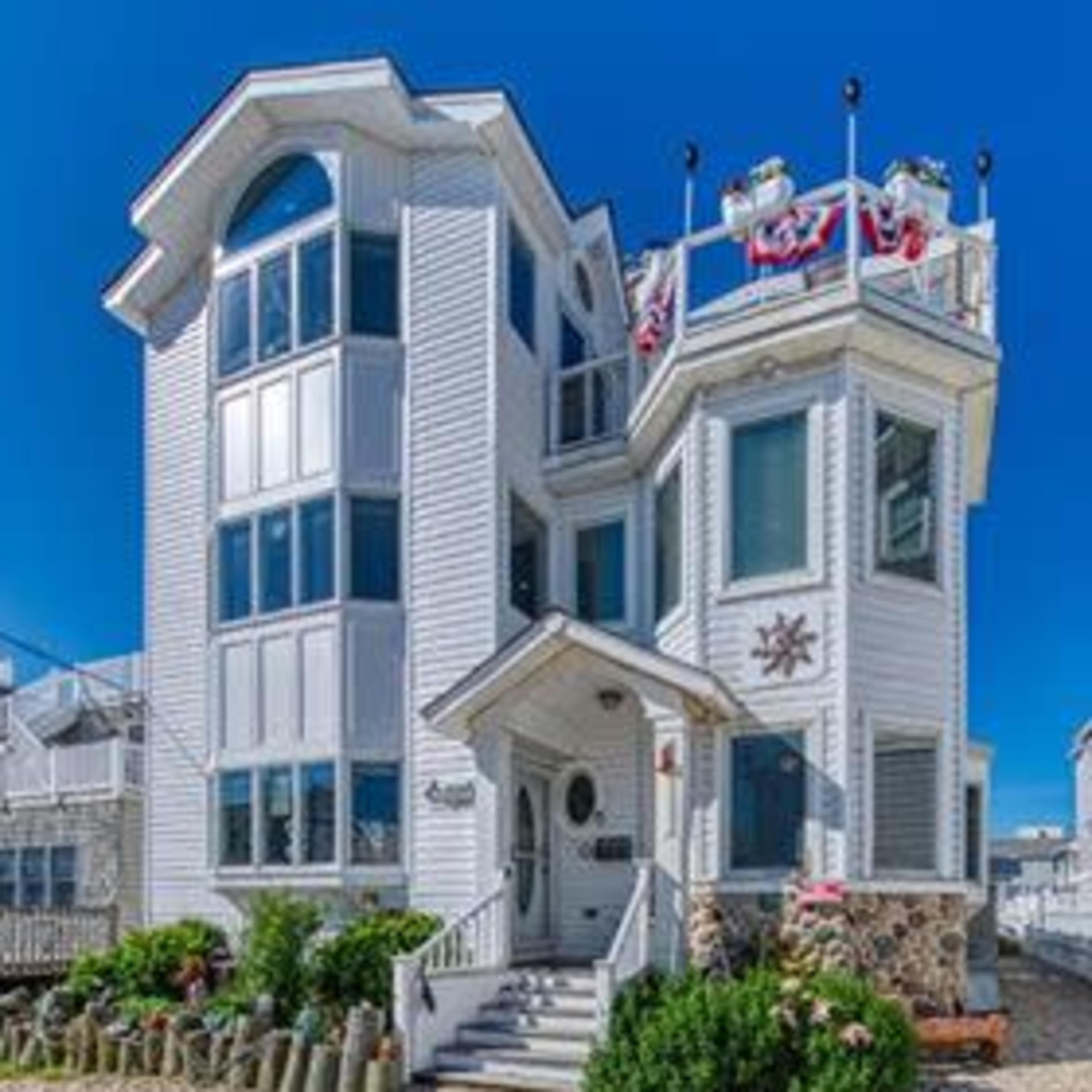 A three-story seaside house with a modern design, featuring large windows and a decorative rooftop.