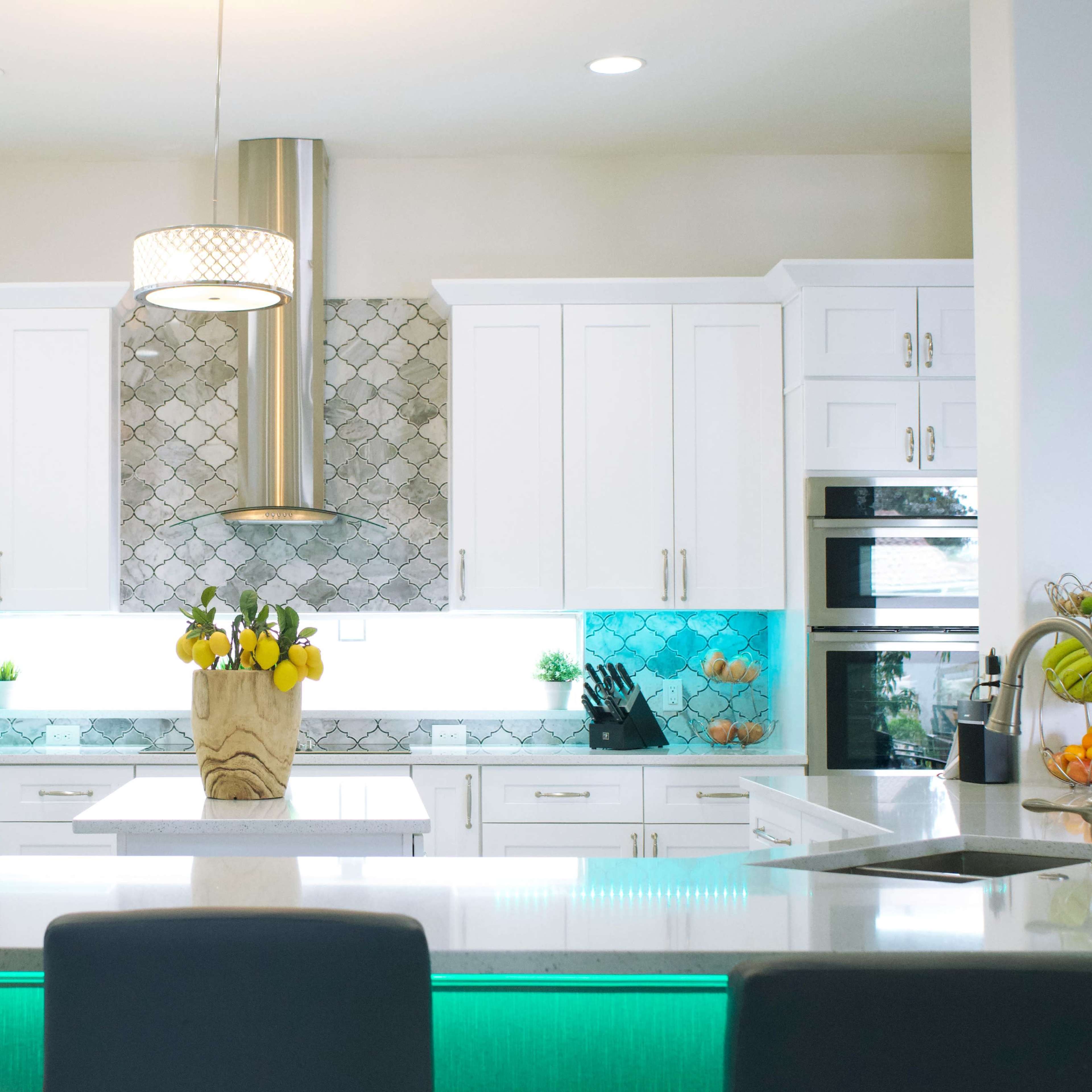 A modern kitchen with white cabinetry, a large island with a light countertop, and vibrant blue tile backsplash under a stylish hood.