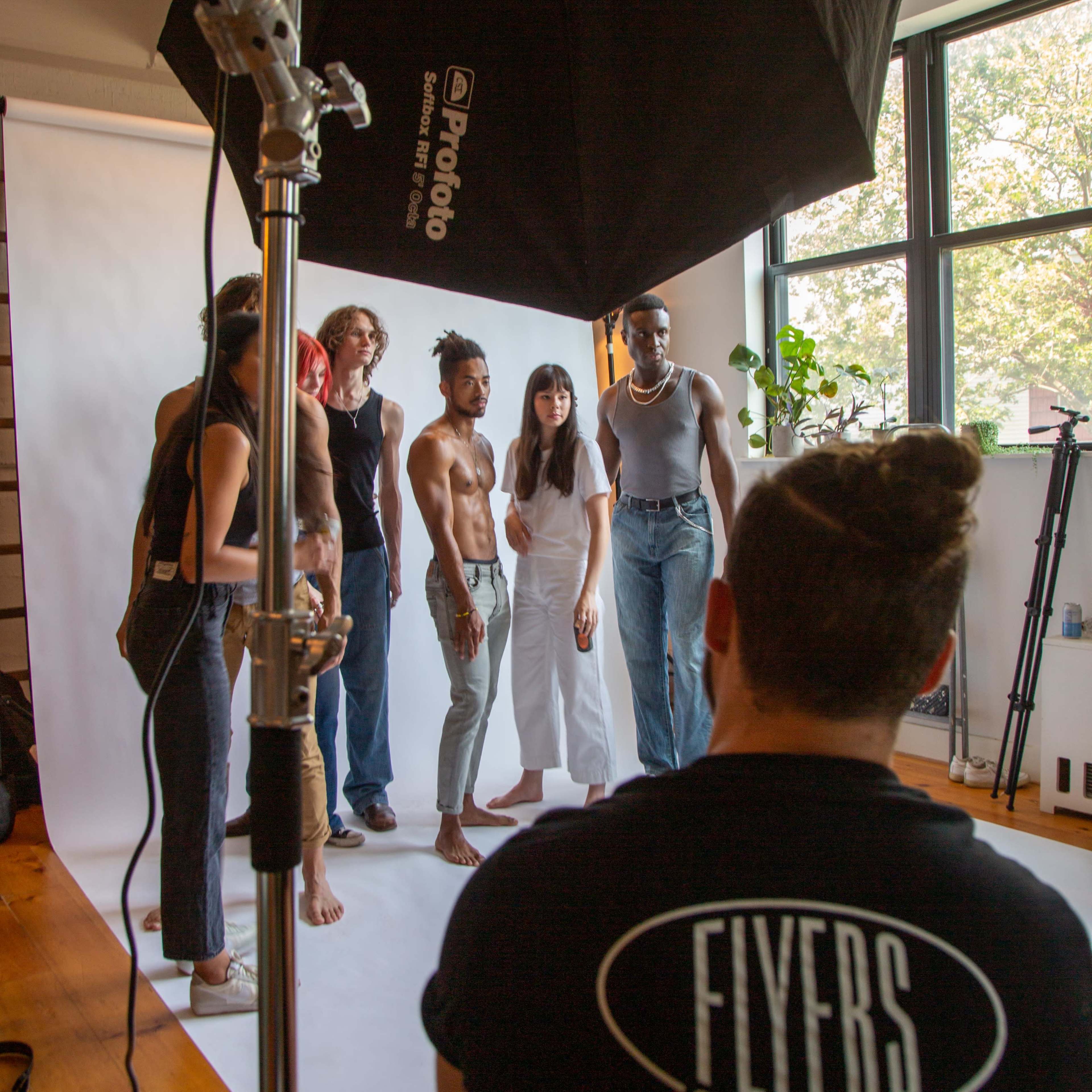 A group of seven people is posing for a photoshoot in a brightly lit studio with a large softbox overhead.