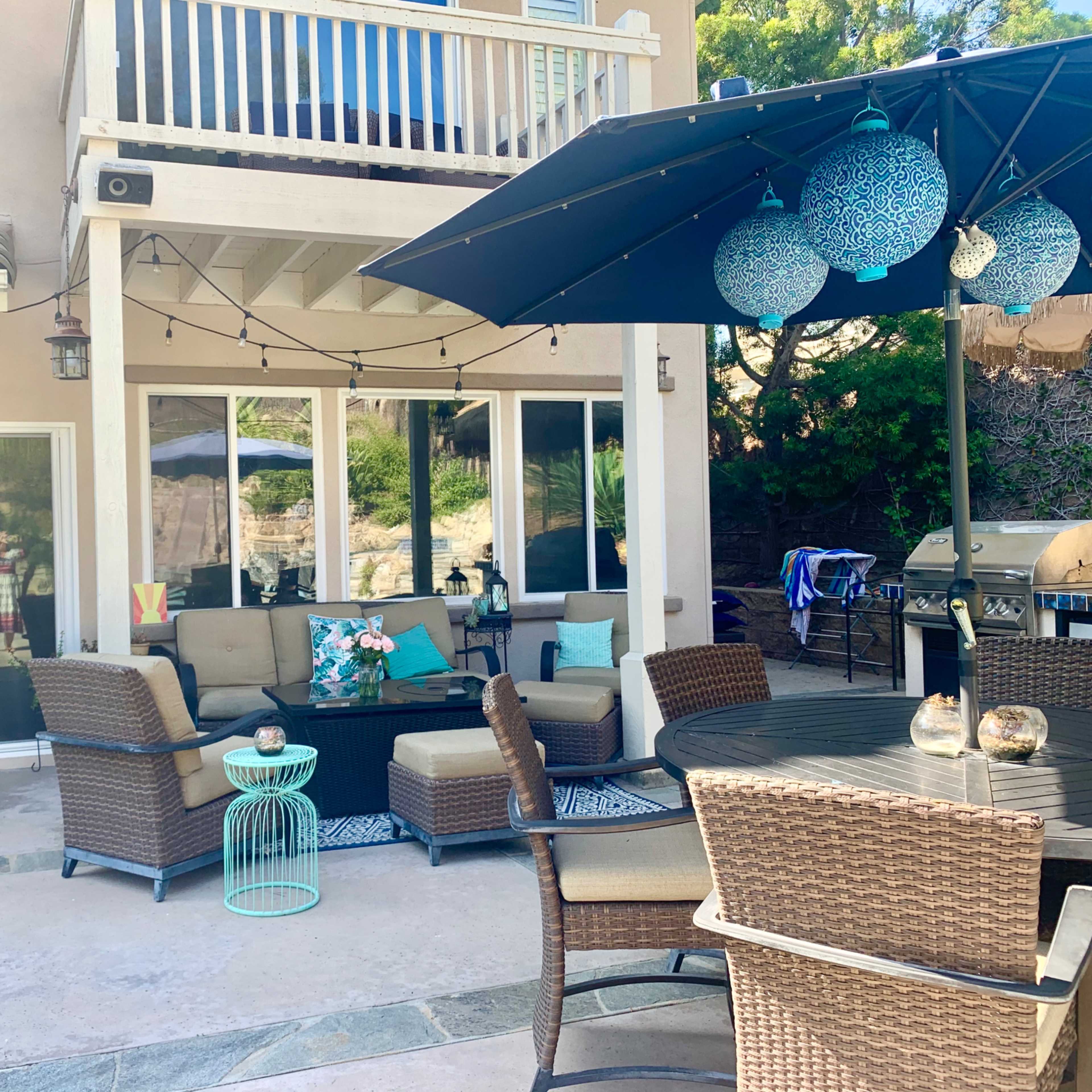 A backyard patio area with a seating arrangement, an umbrella, and a barbecue grill.