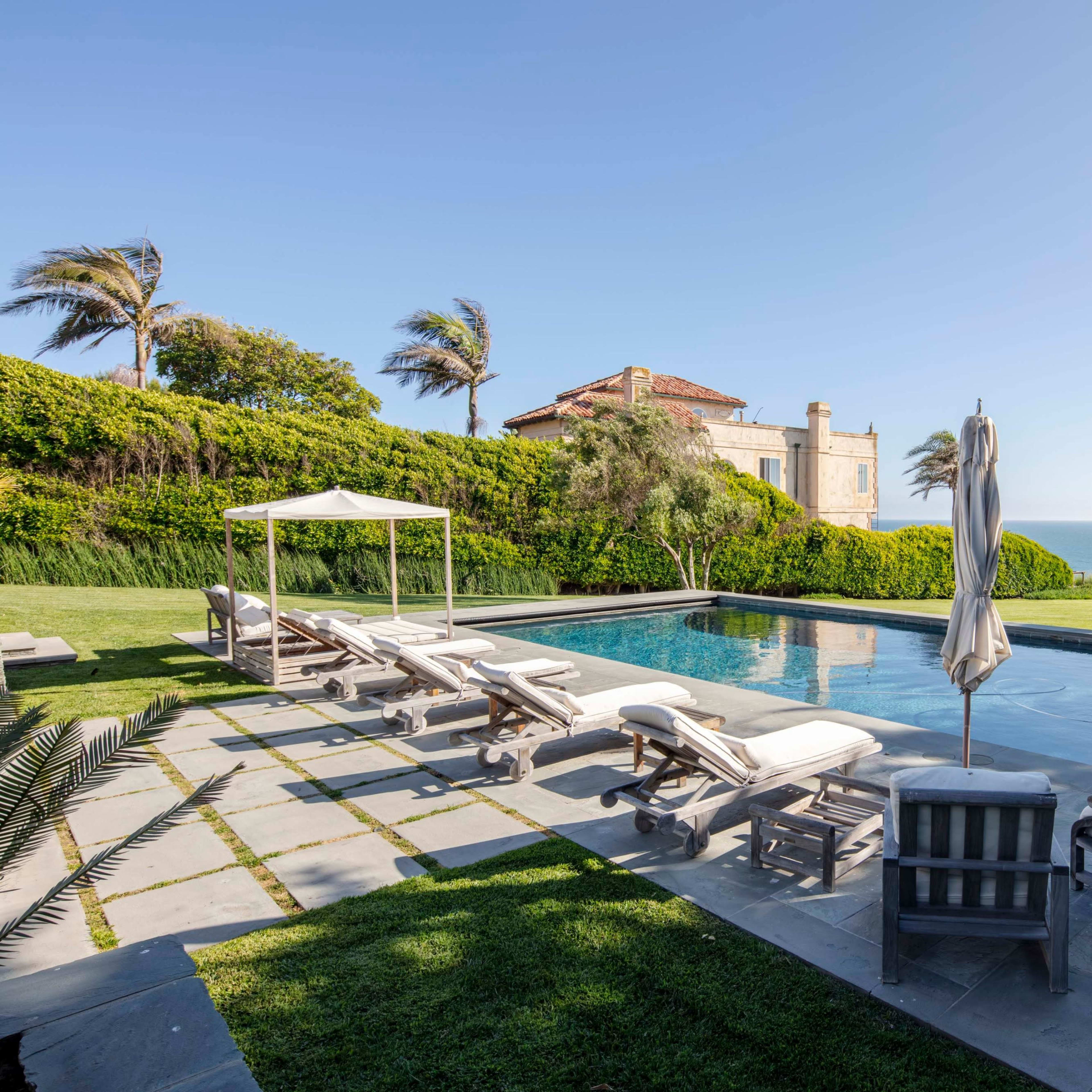 A landscaped pool area with lounge chairs and a cabana overlooking the ocean.