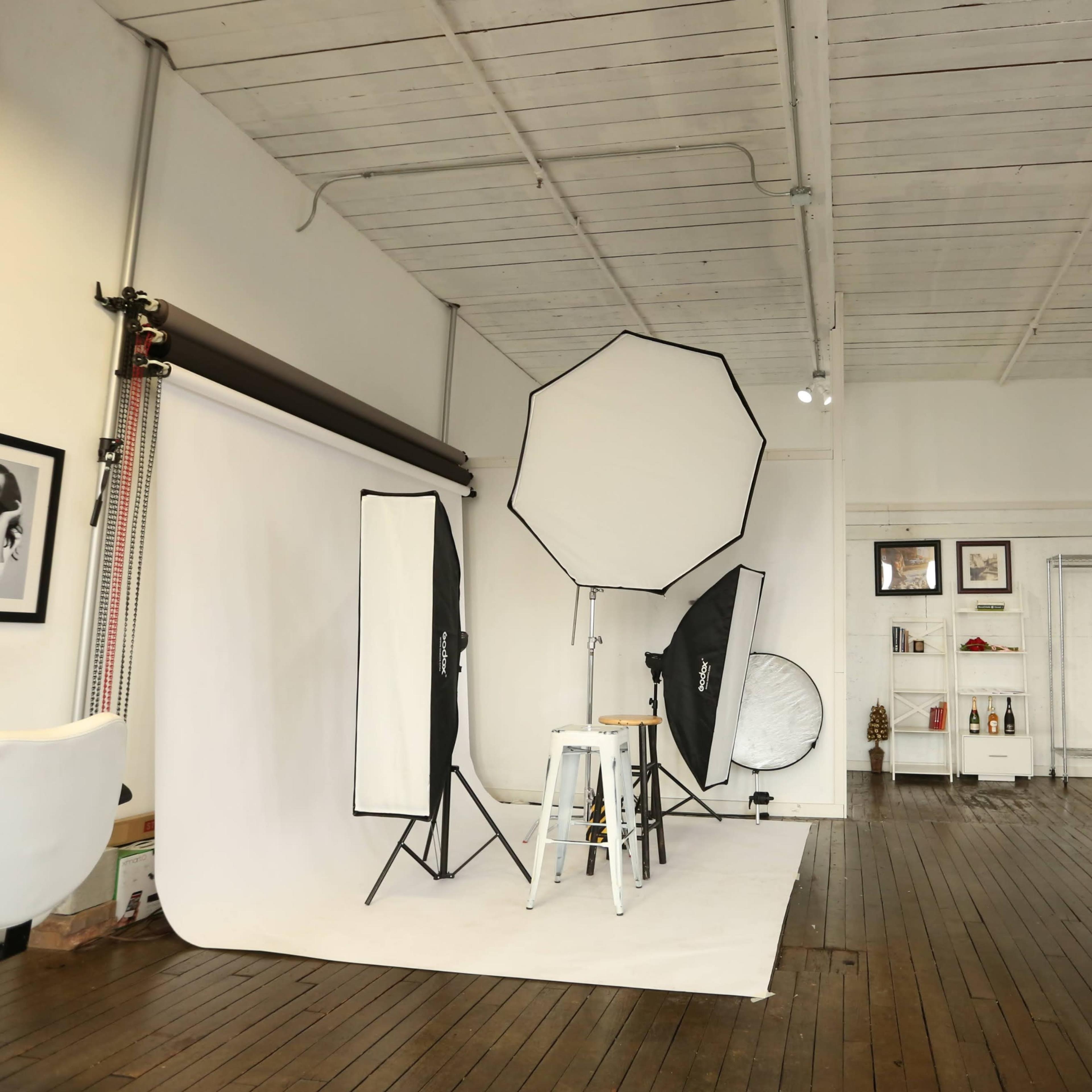 A photography studio with a white backdrop, lighting equipment, and wooden floors.